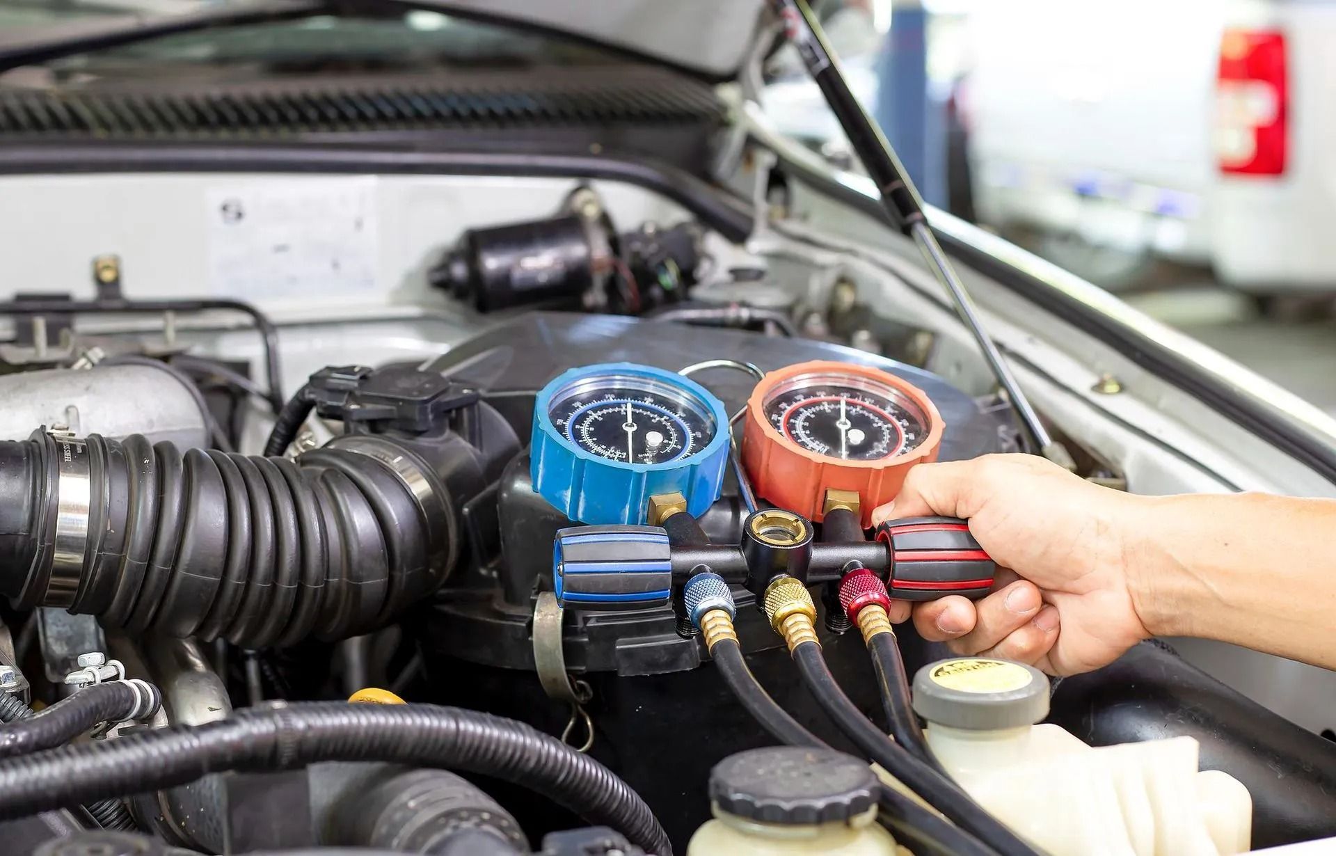 Mechanic checking car engine with blue and orange gauge manifold attached to air conditioning hoses
