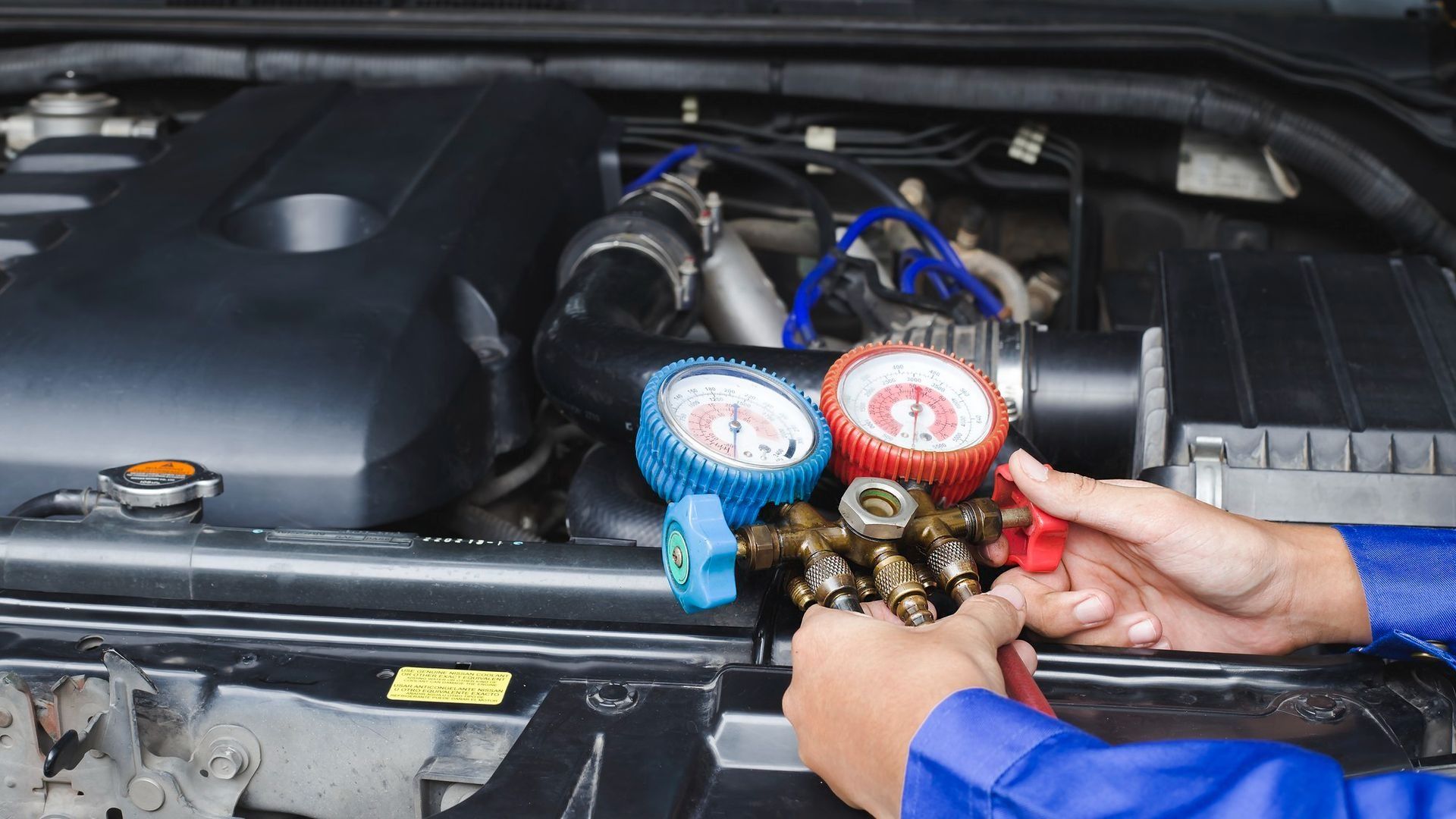 Hands holding blue and red manifold gauges on a car engine in the engine bay