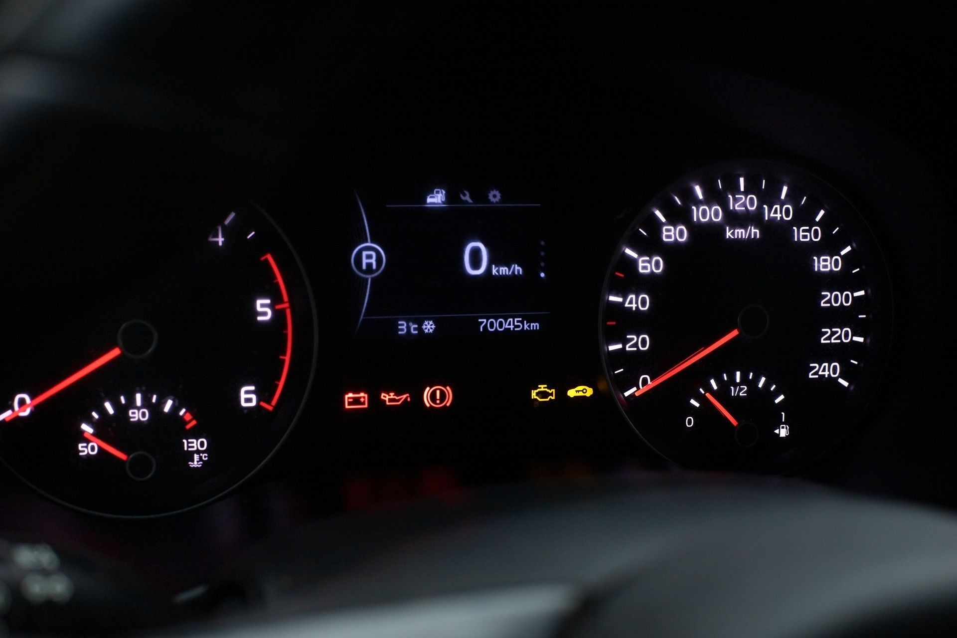 Car dashboard at night showing illuminated speedometer, gauges, and warning lights with 0 mph on the display