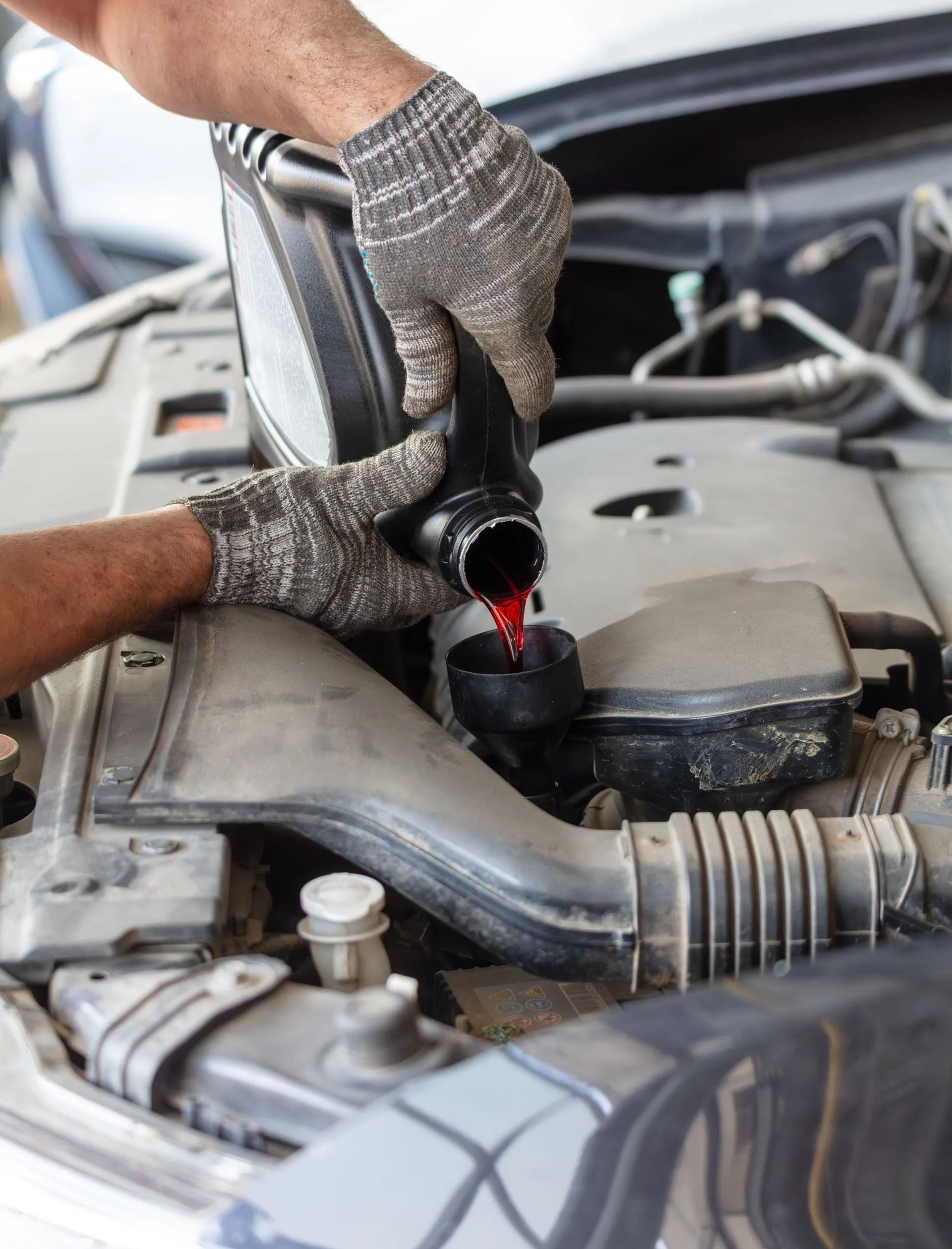 Mechanic pouring red fluid into a car engine reservoir under the hood