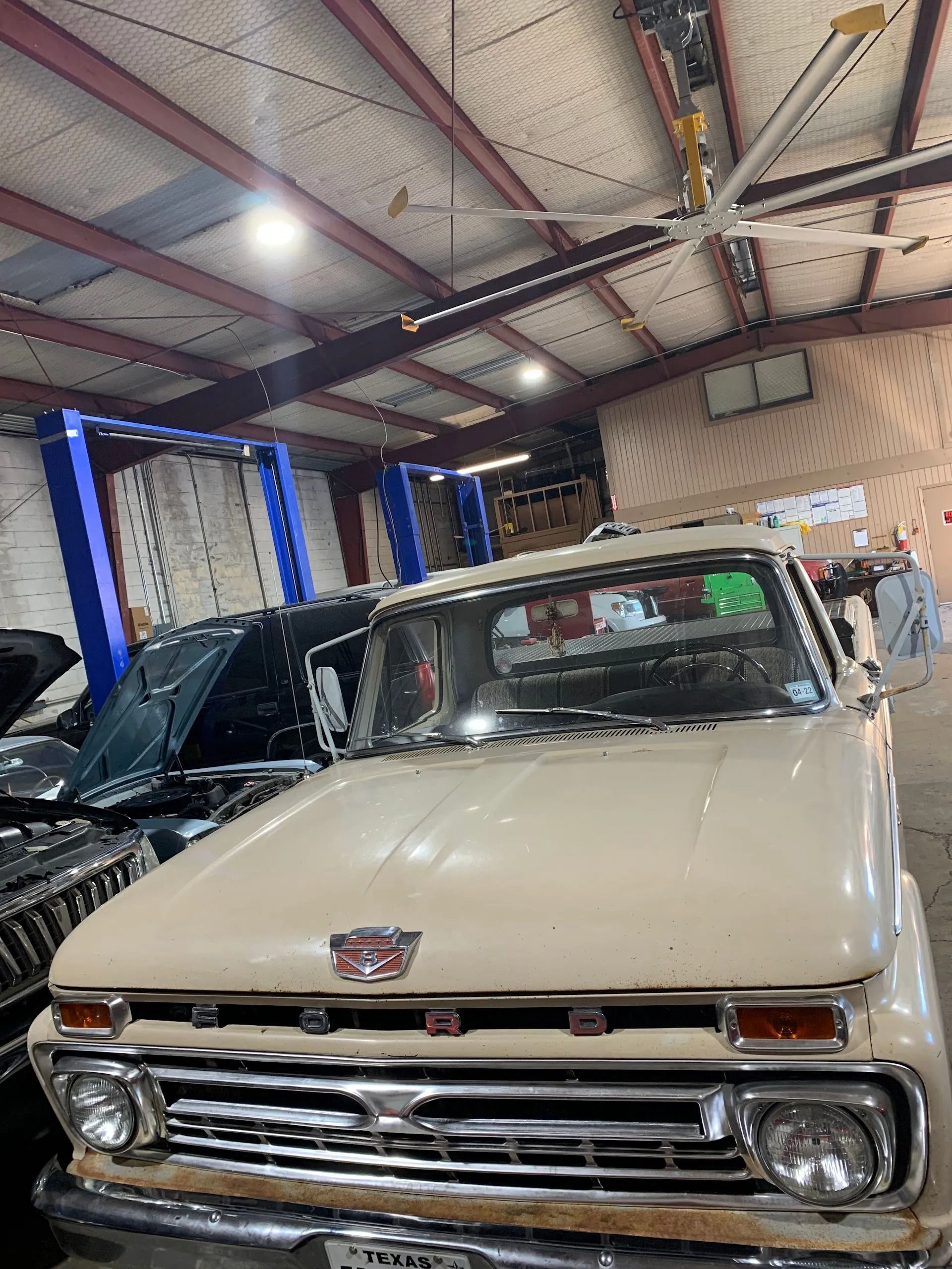 Classic beige car displayed indoors in an auto shop, front view