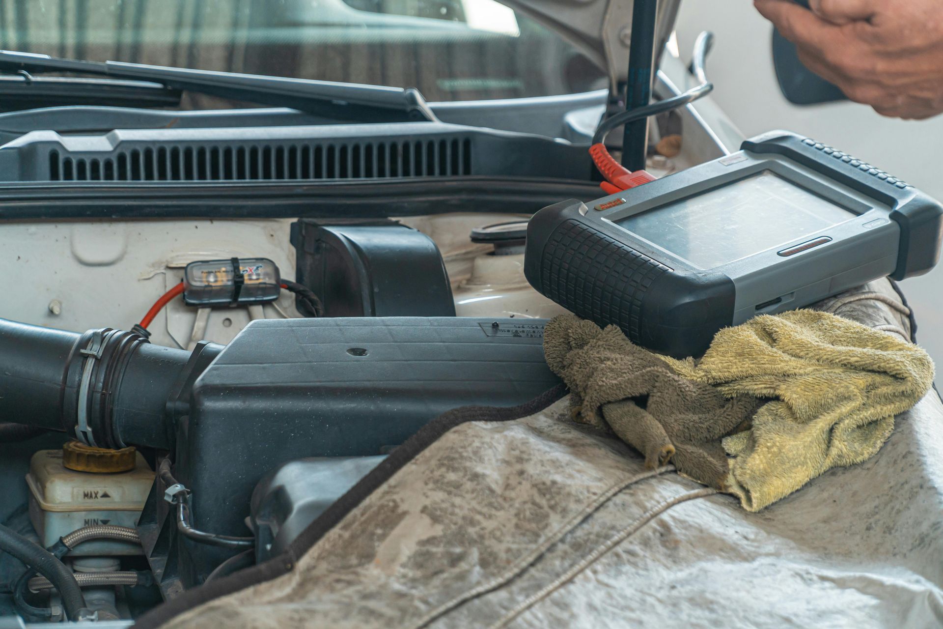 Black car dashboard/engine bay area with a dirty cloth and plastic tray on top near the windshield.