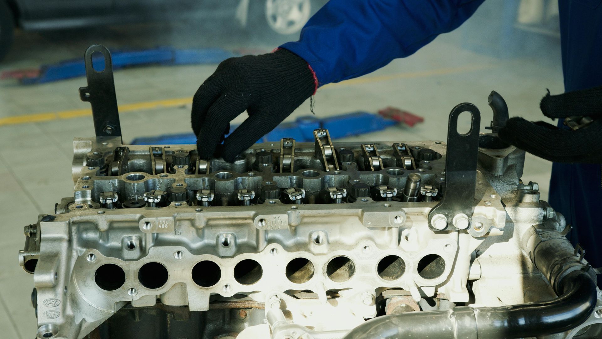 Mechanic in blue jacket adjusts an engine cylinder head on a workbench