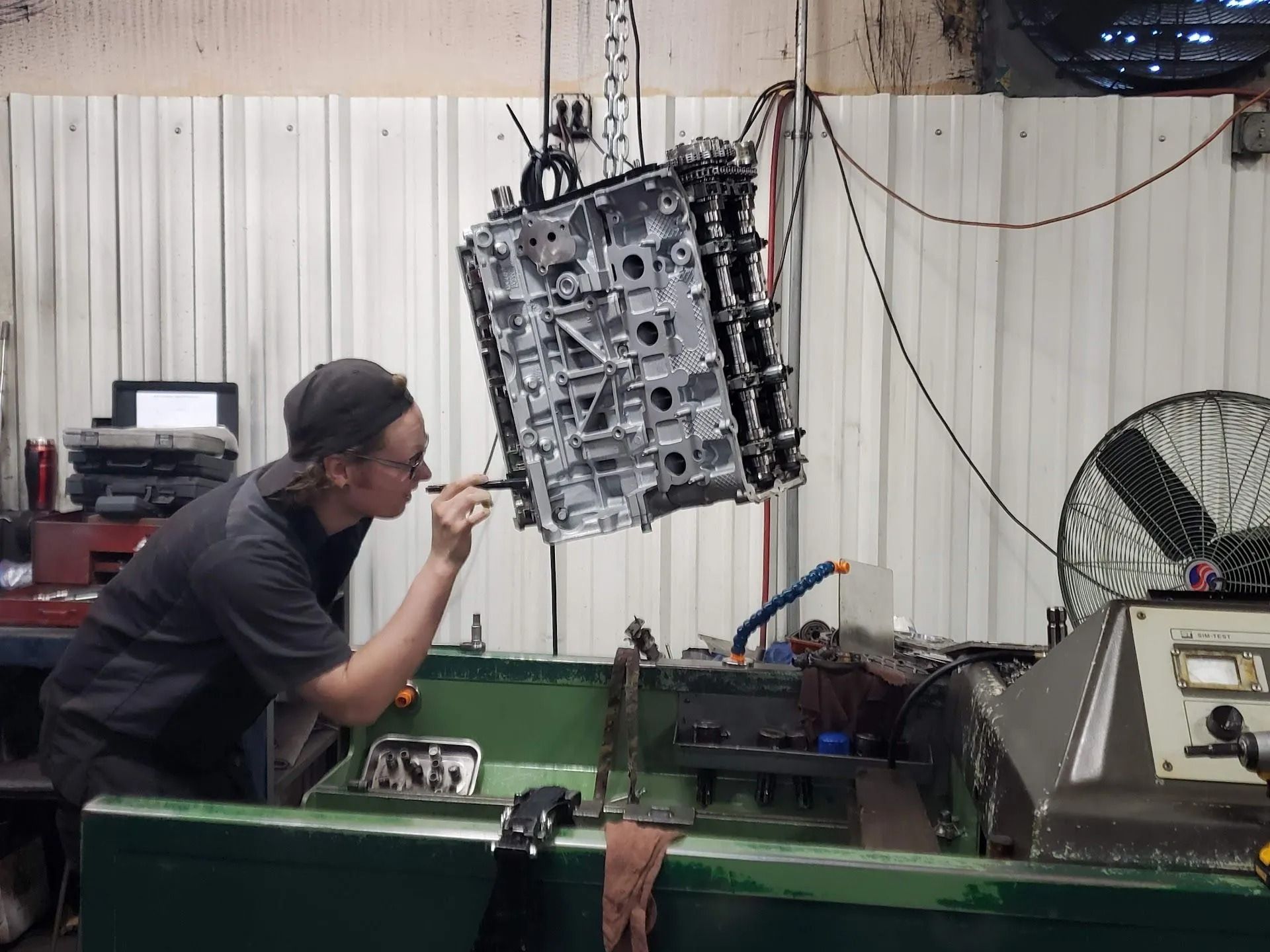 Mechanic inspecting a hanging engine block in a workshop with tools and machinery nearby
