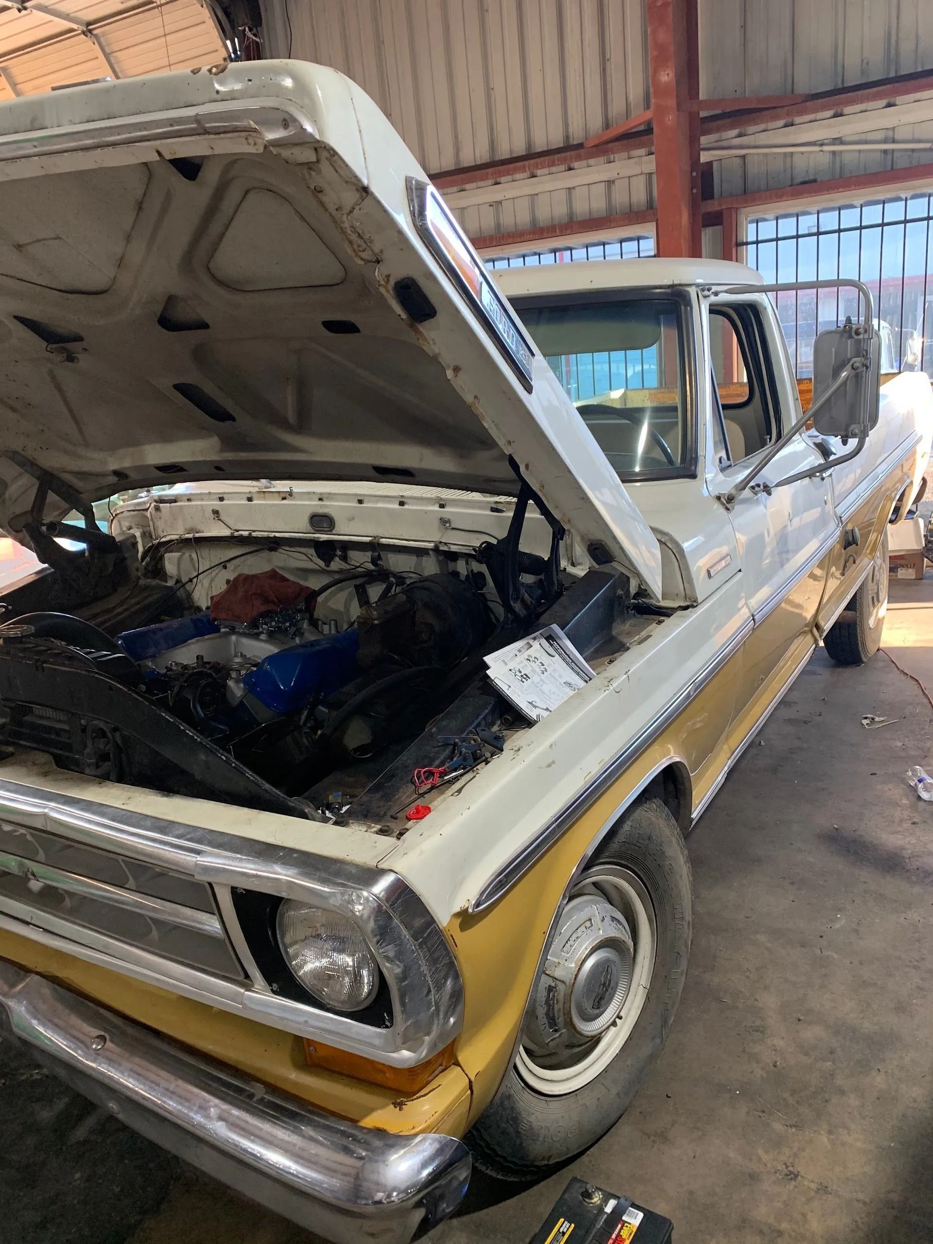 Vintage yellow pickup with open hood in a garage, showing engine bay and worn interior.