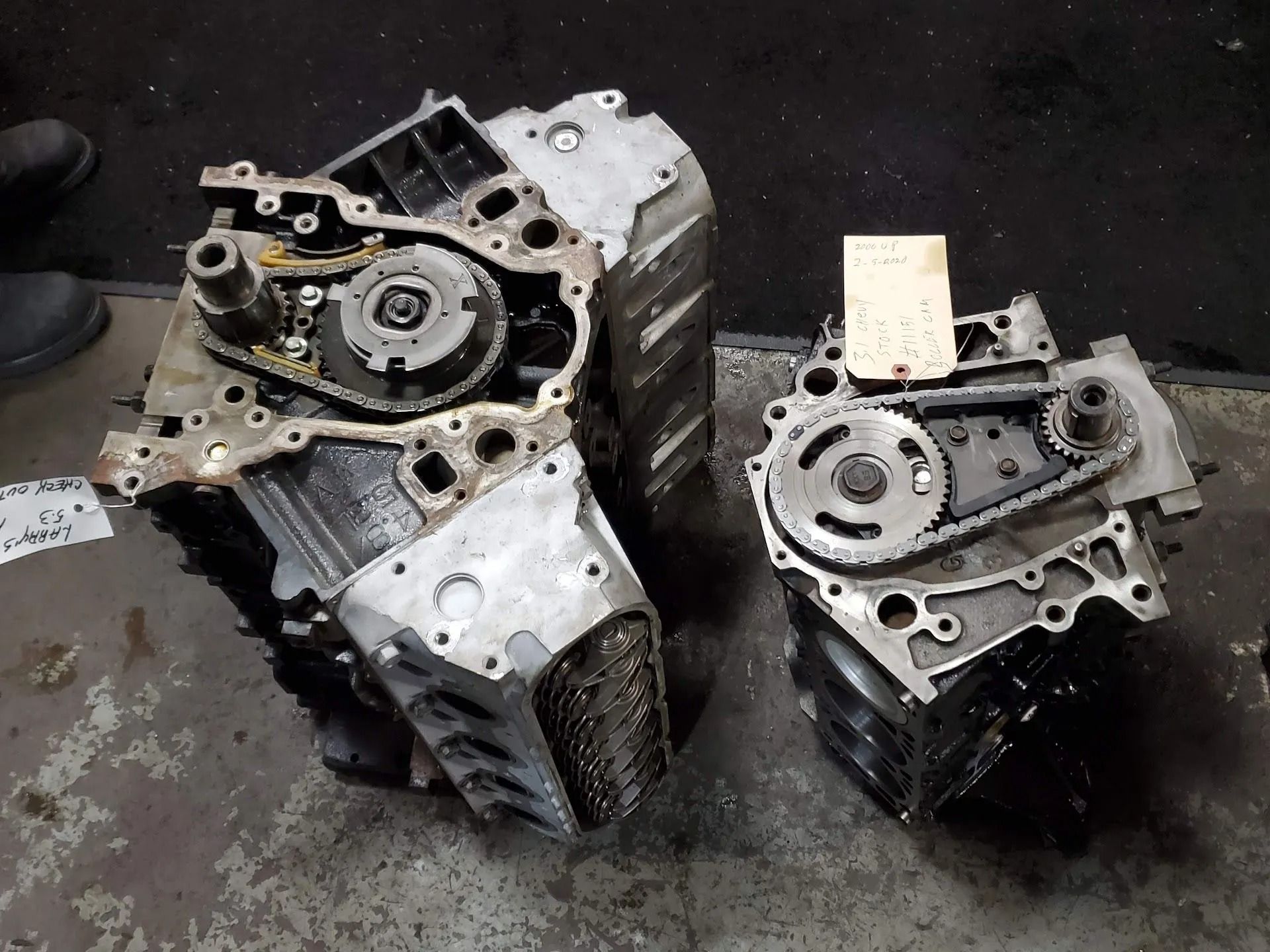 Two metal engine blocks with exposed gears and housings on a dark surface.