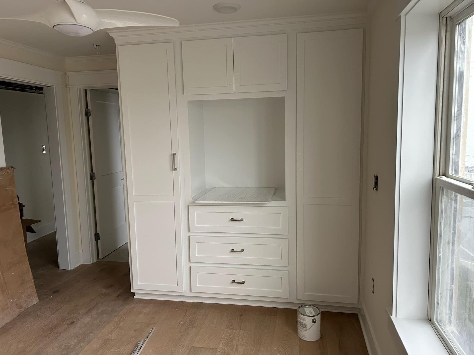 A room with white cabinets and drawers and a window