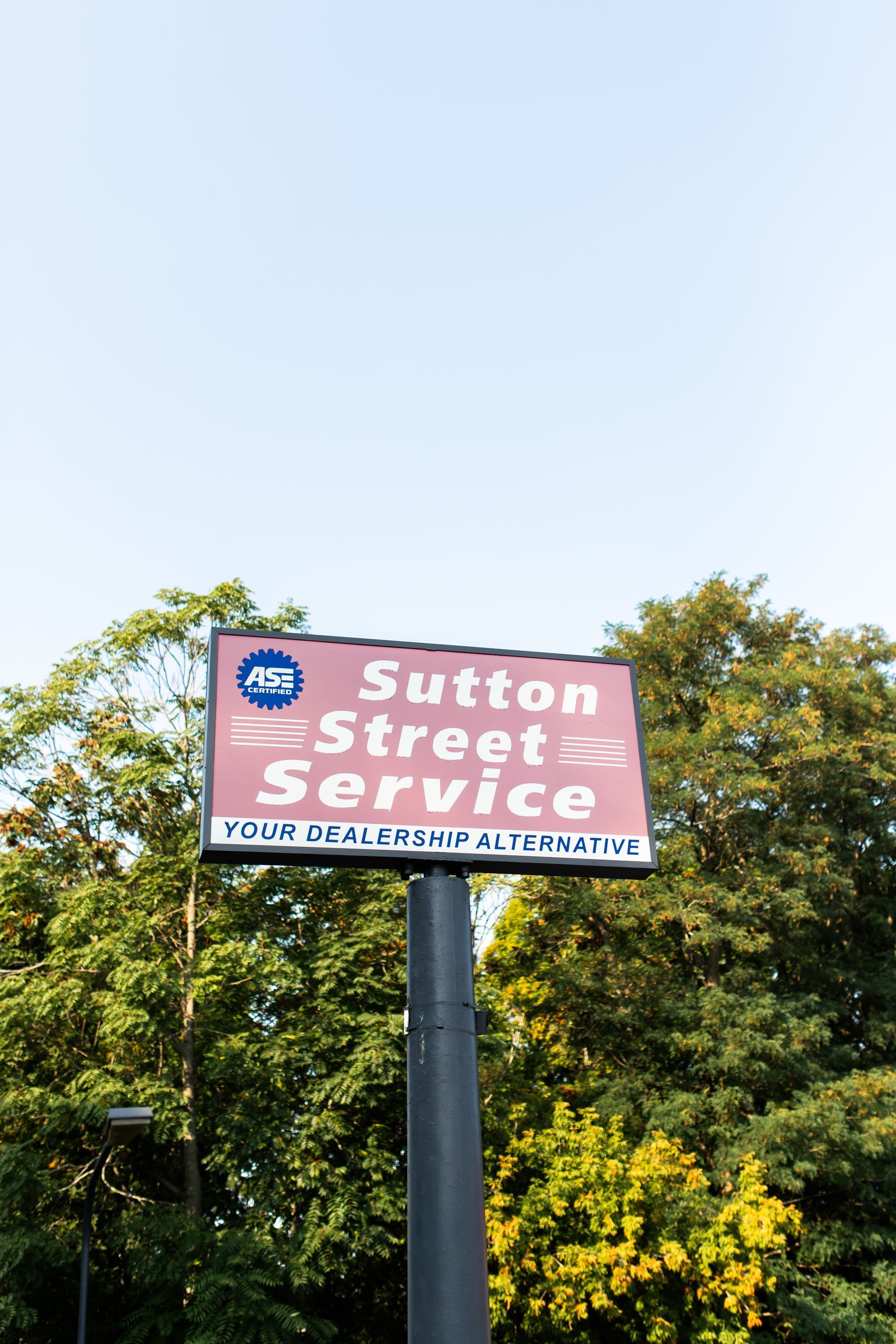 Street service sign on a pole with pink background, against trees and blue sky.