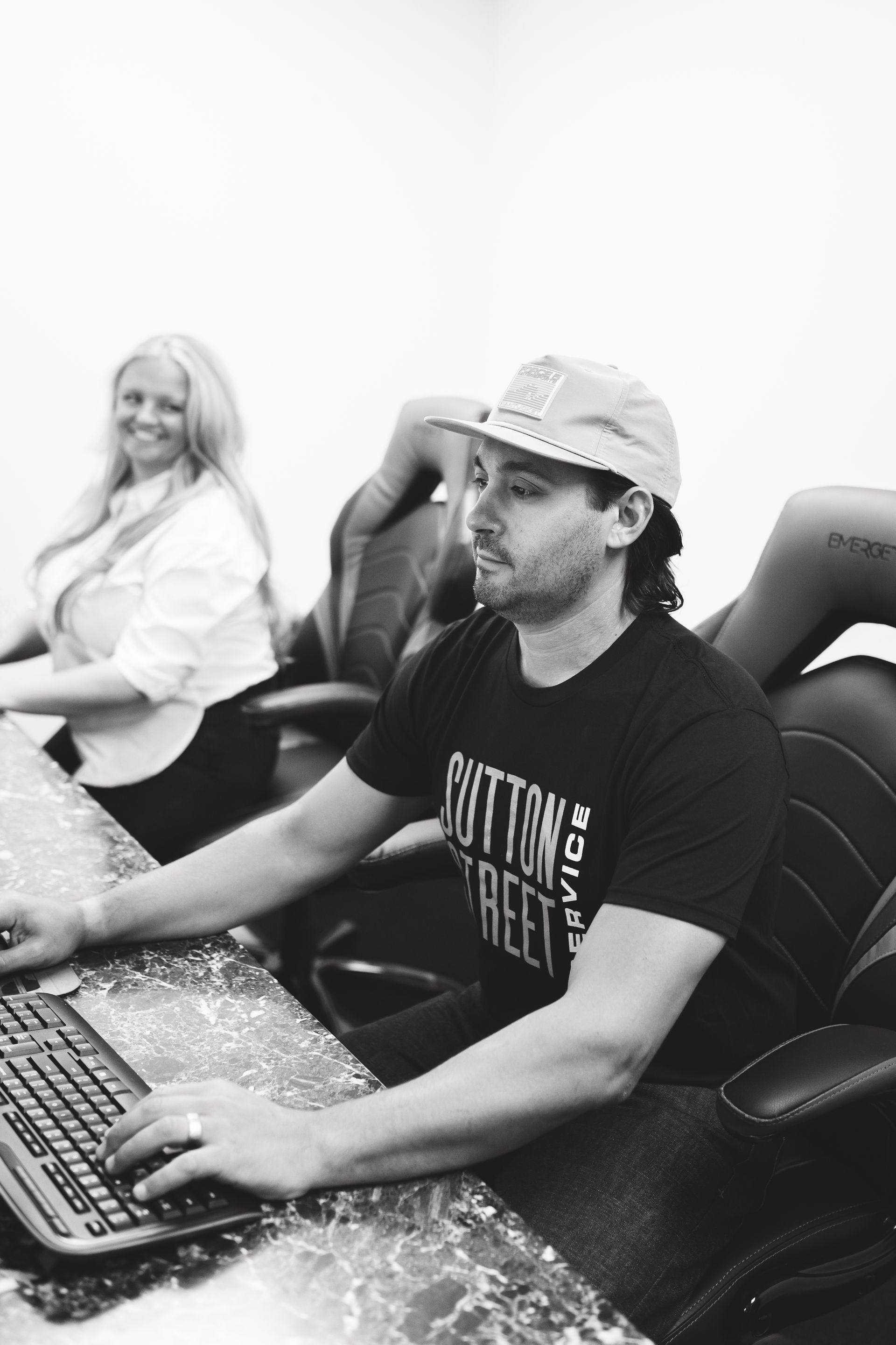 Two people seated at computer workstations, one typing at a keyboard in the foreground.