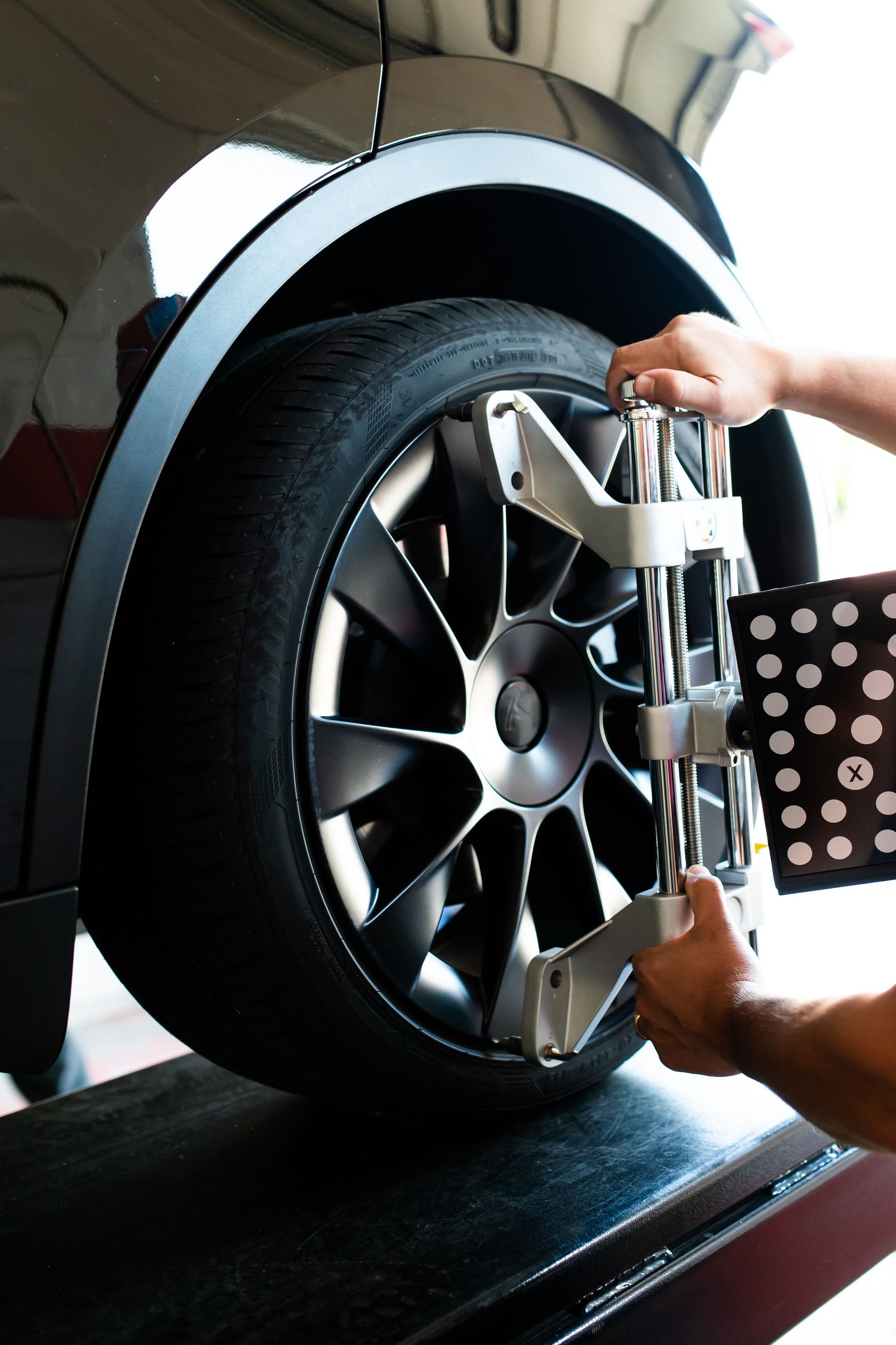 Hands adjusting a silver wheel clamp on a black car tire in a garage