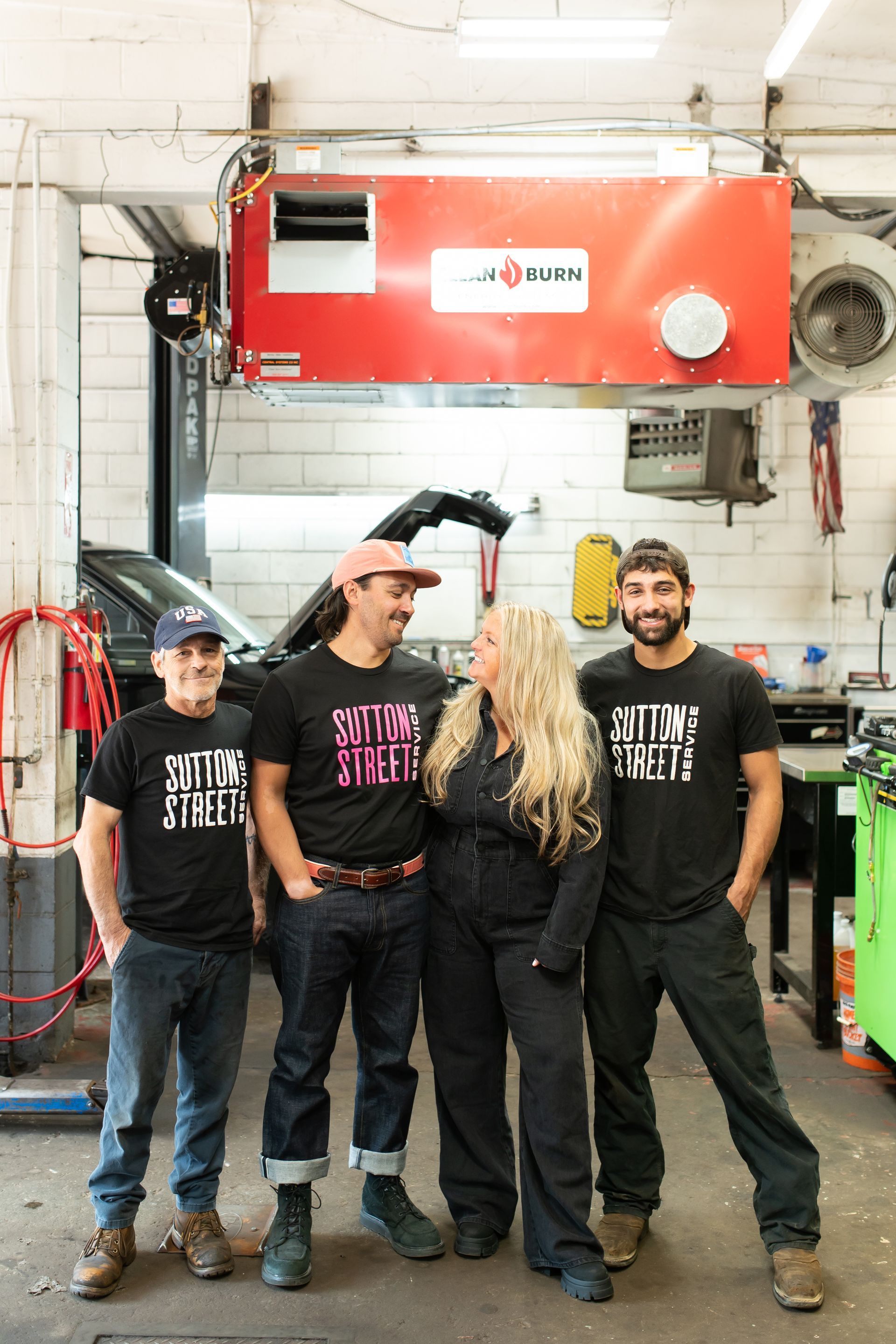 Four people posing in a workshop, standing in front of a red machine and tools