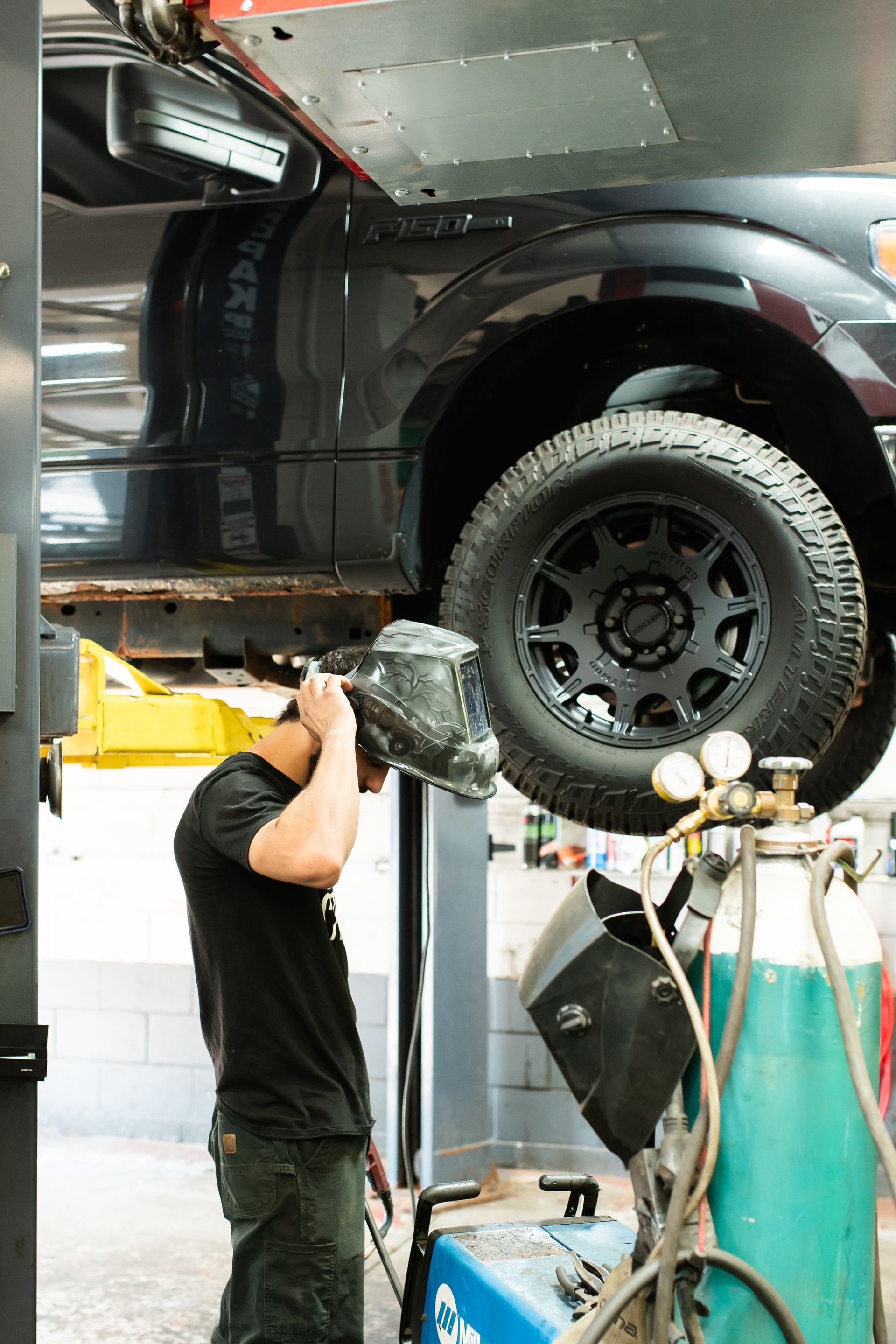Mechanic inspecting a lifted black truck in an auto repair shop