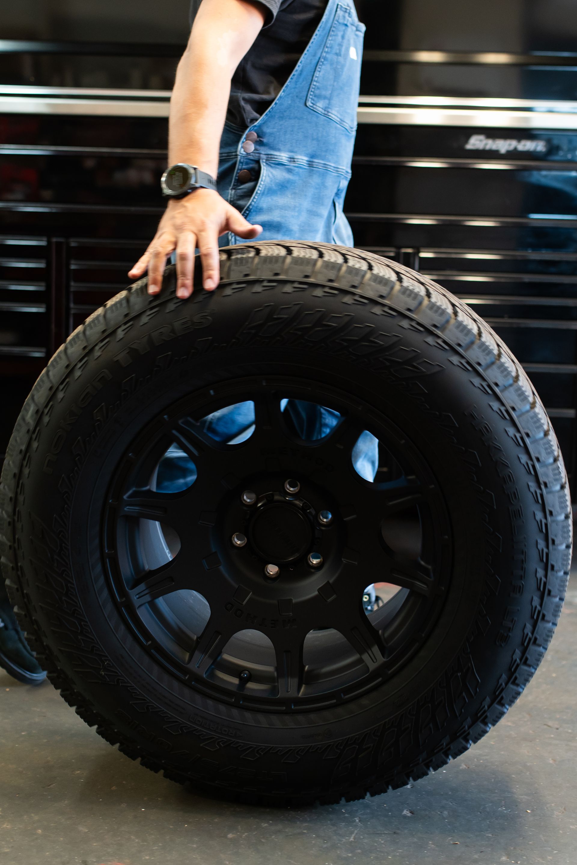Person holding a large black tire with a blue vehicle in the background