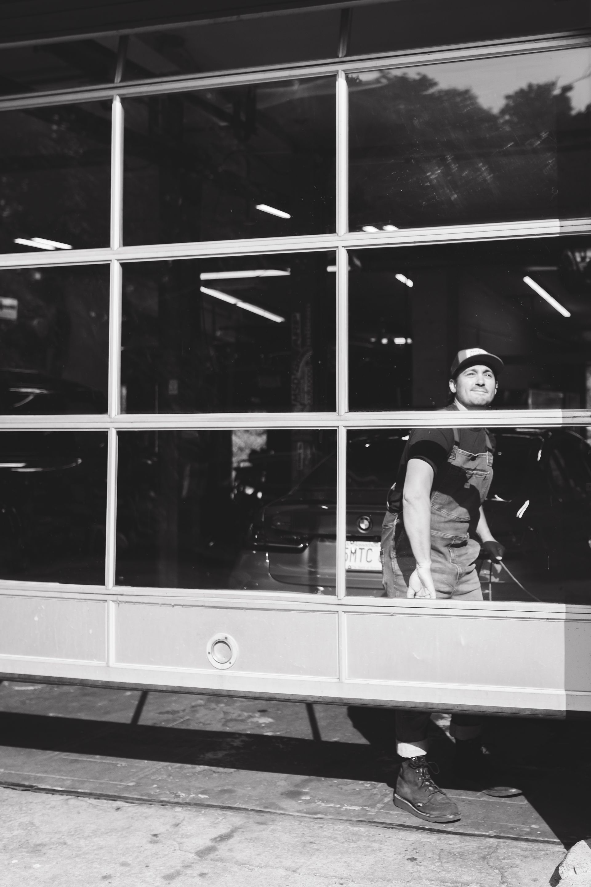 Person standing outside a large windowed building, wearing a cap and backpack.