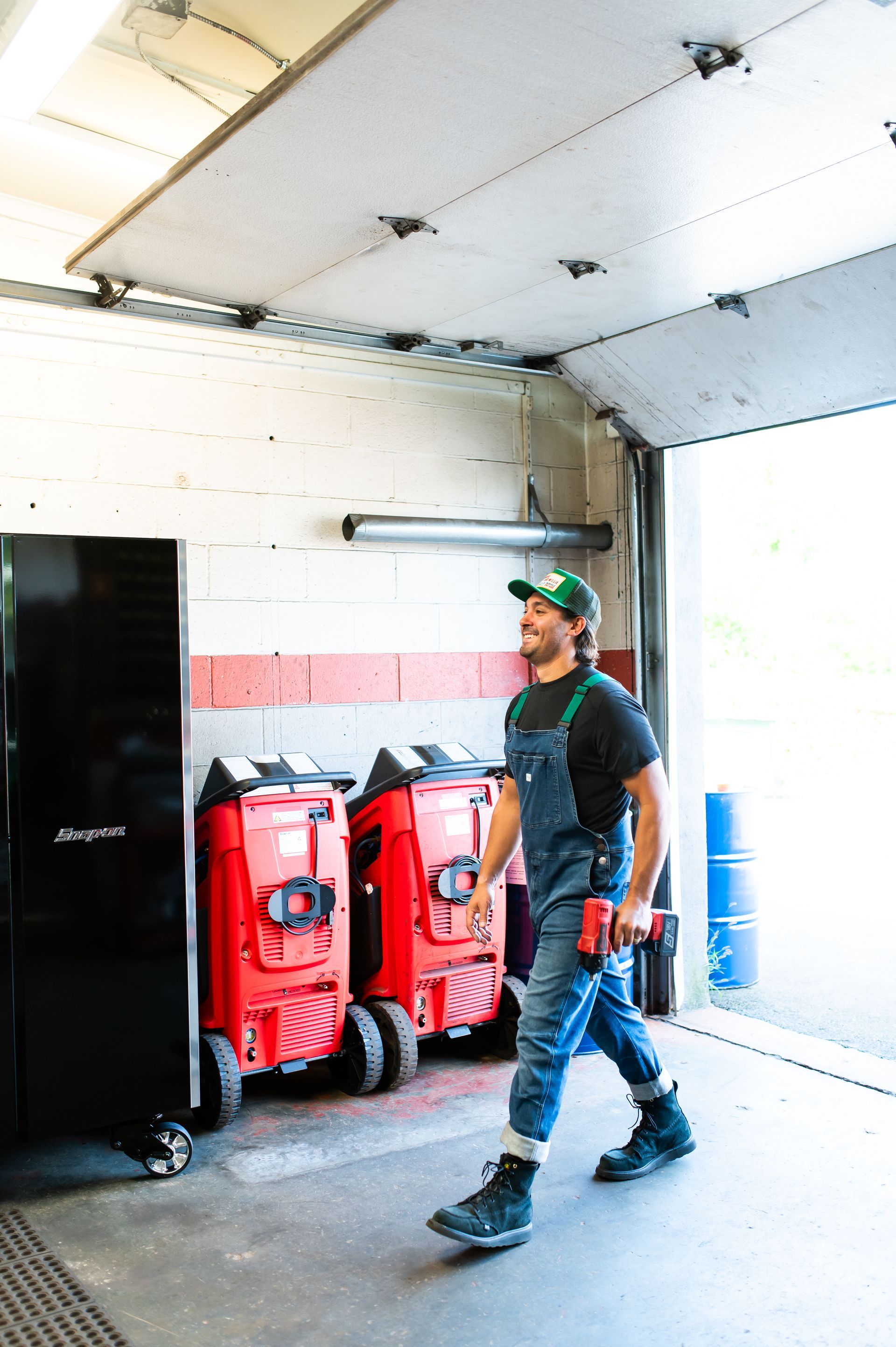 Worker in a garage near red equipment and a black cabinet, walking past an open door.