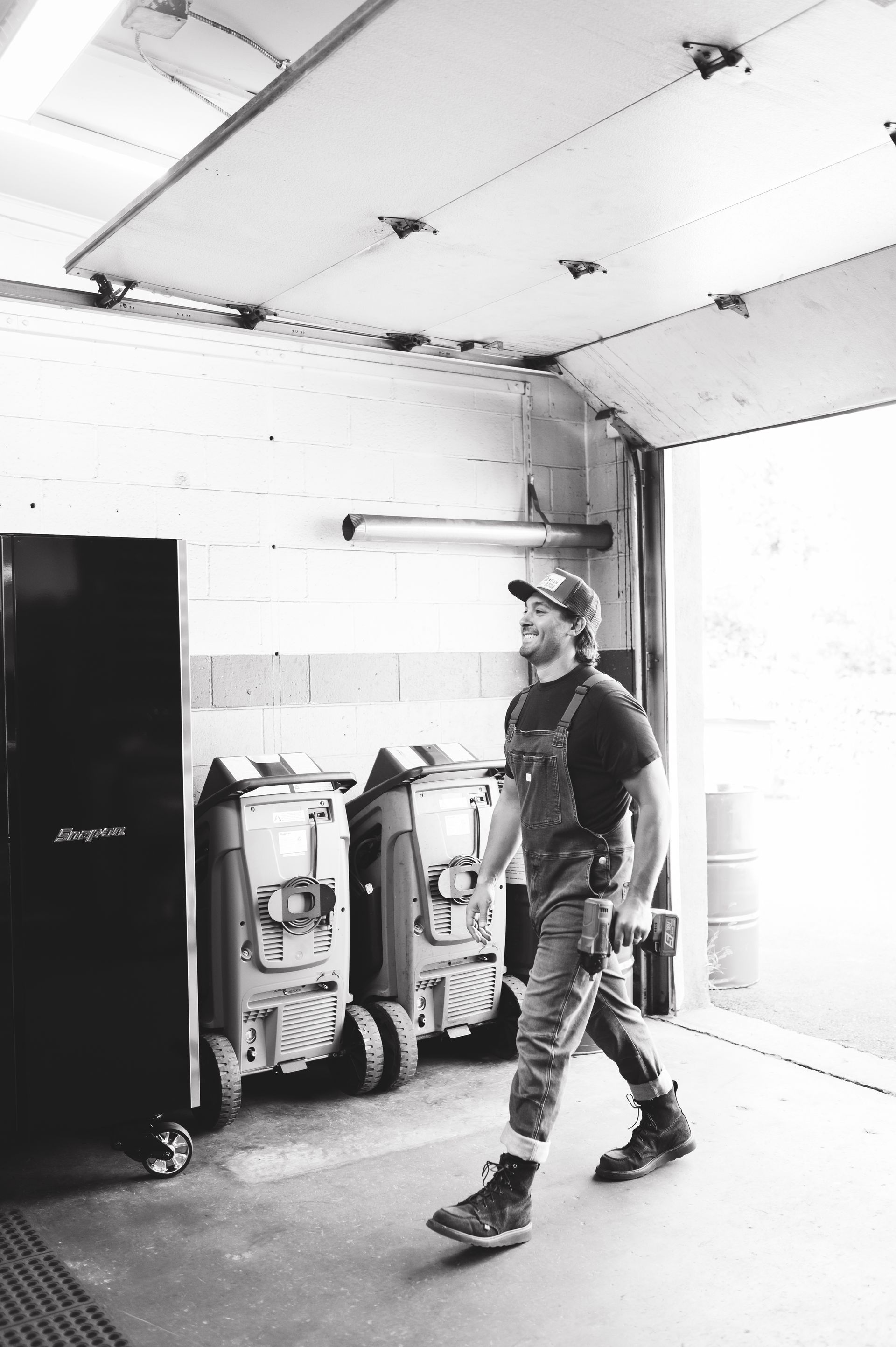 Worker walking through a garage with tools, equipment, and an open door to the right