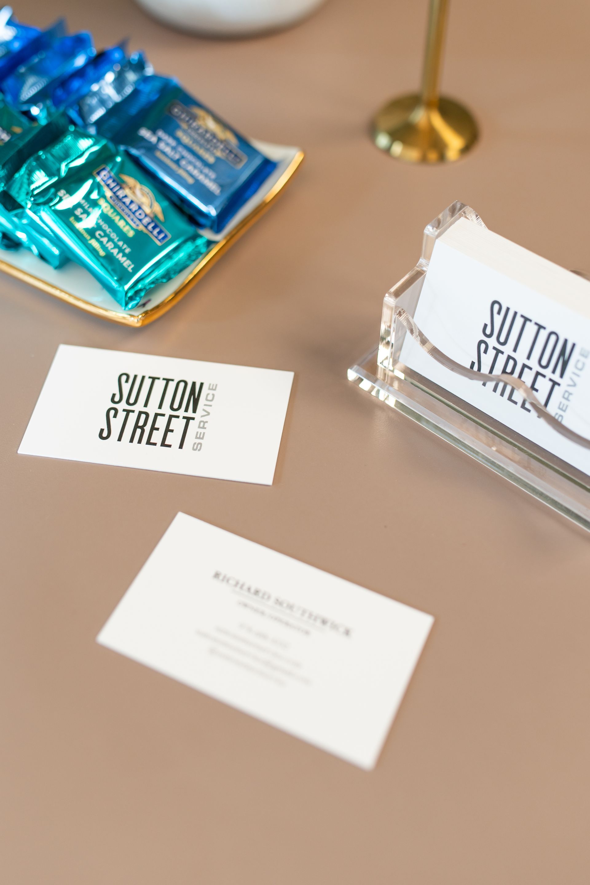 Table with Button Street business cards, a clear card holder, and teal wrapped candies on a beige surface.