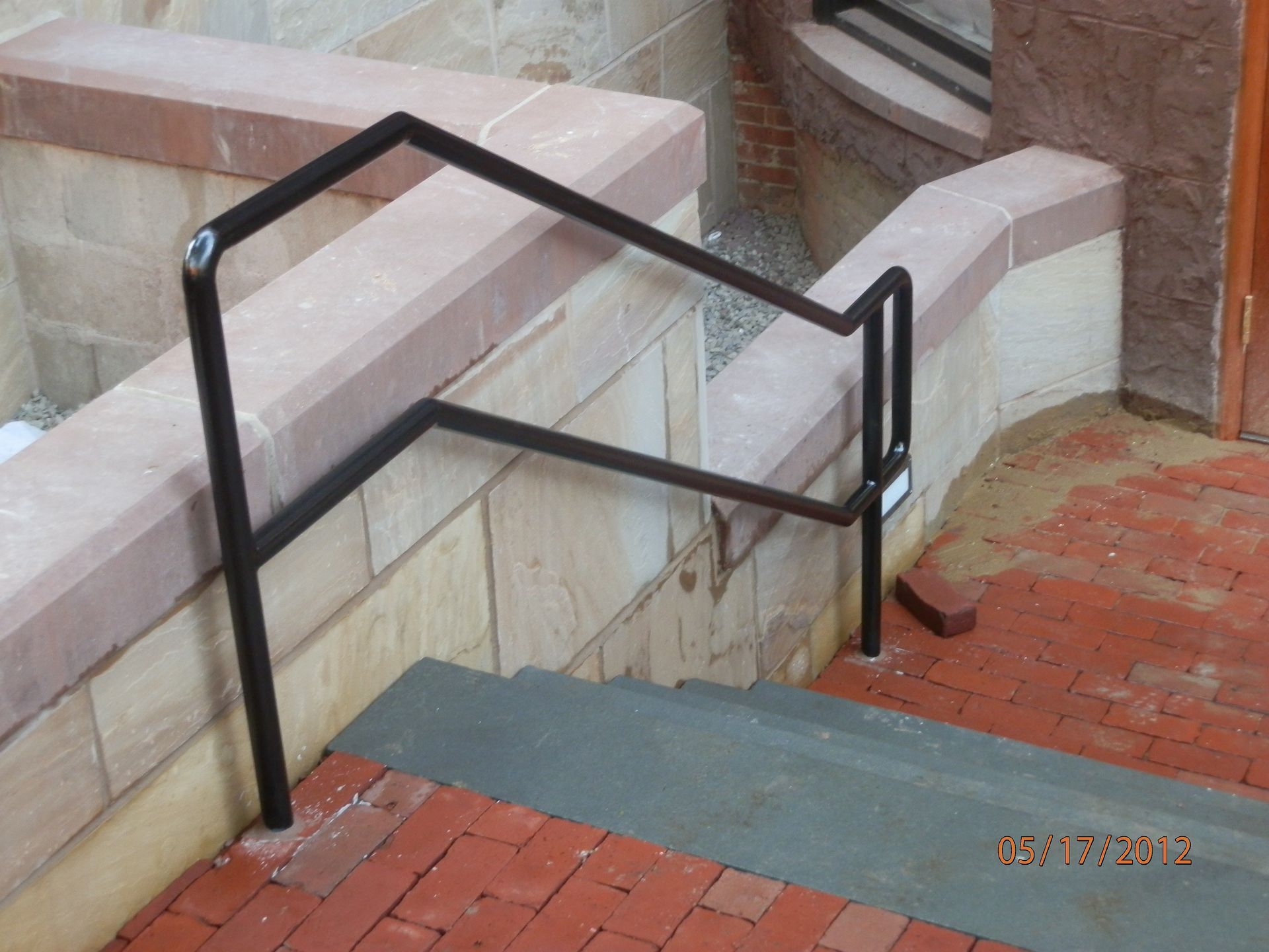 Black metal handrails beside concrete steps and a brick walkway outside a building.