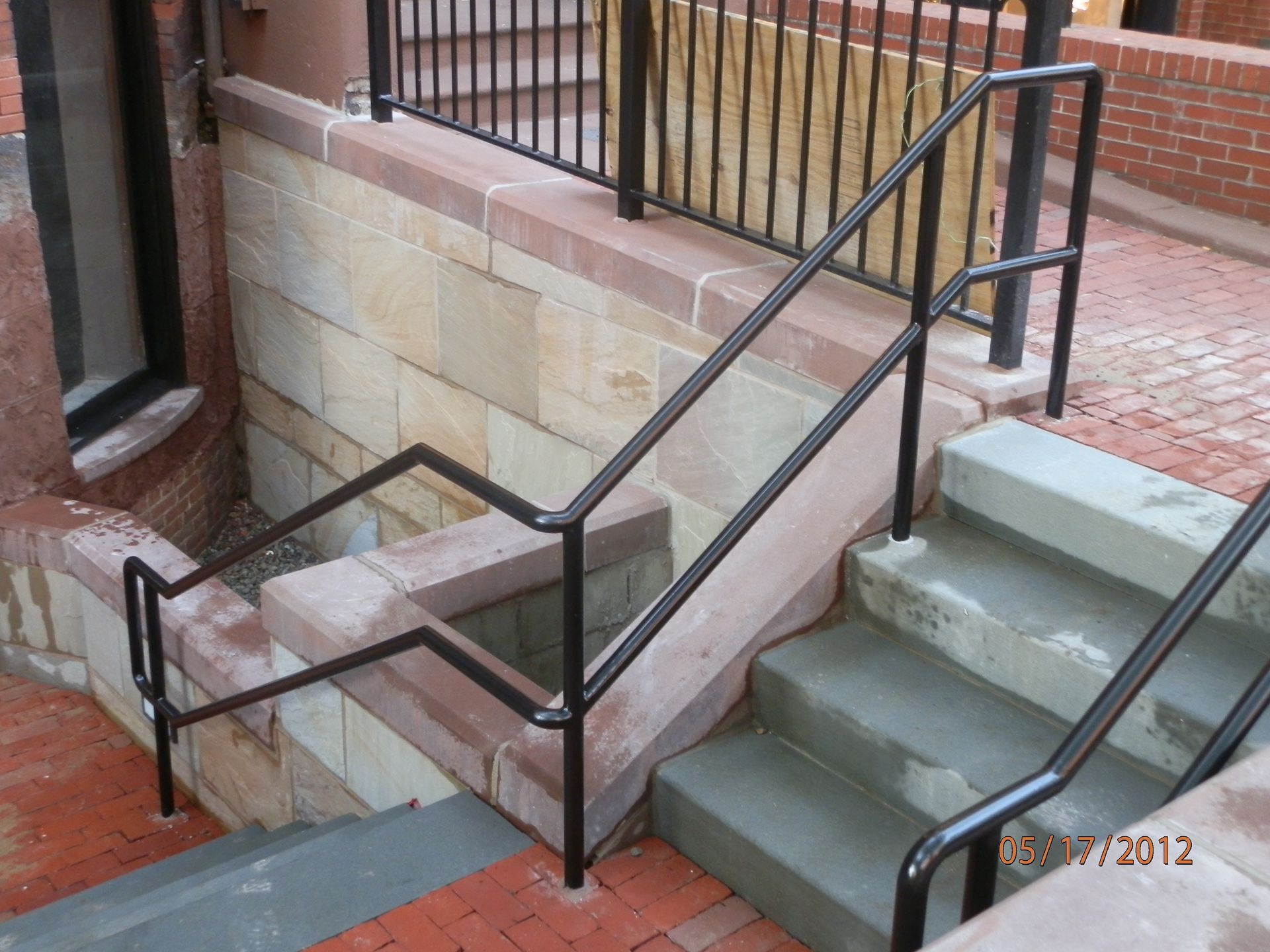 Brick exterior stair ramp with black railings leading to an elevated walkway