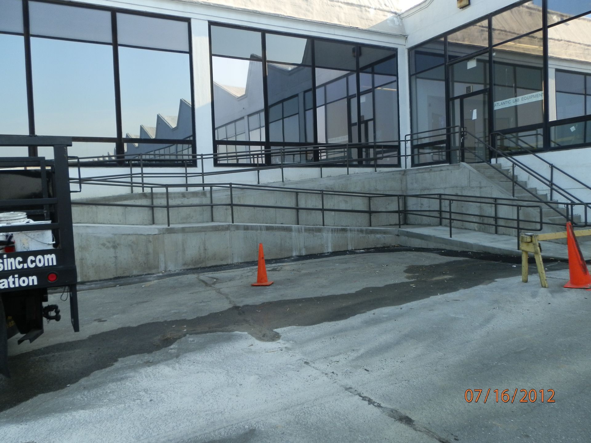 Empty concrete ramp outside a glass building, with orange traffic cones and temporary barriers.