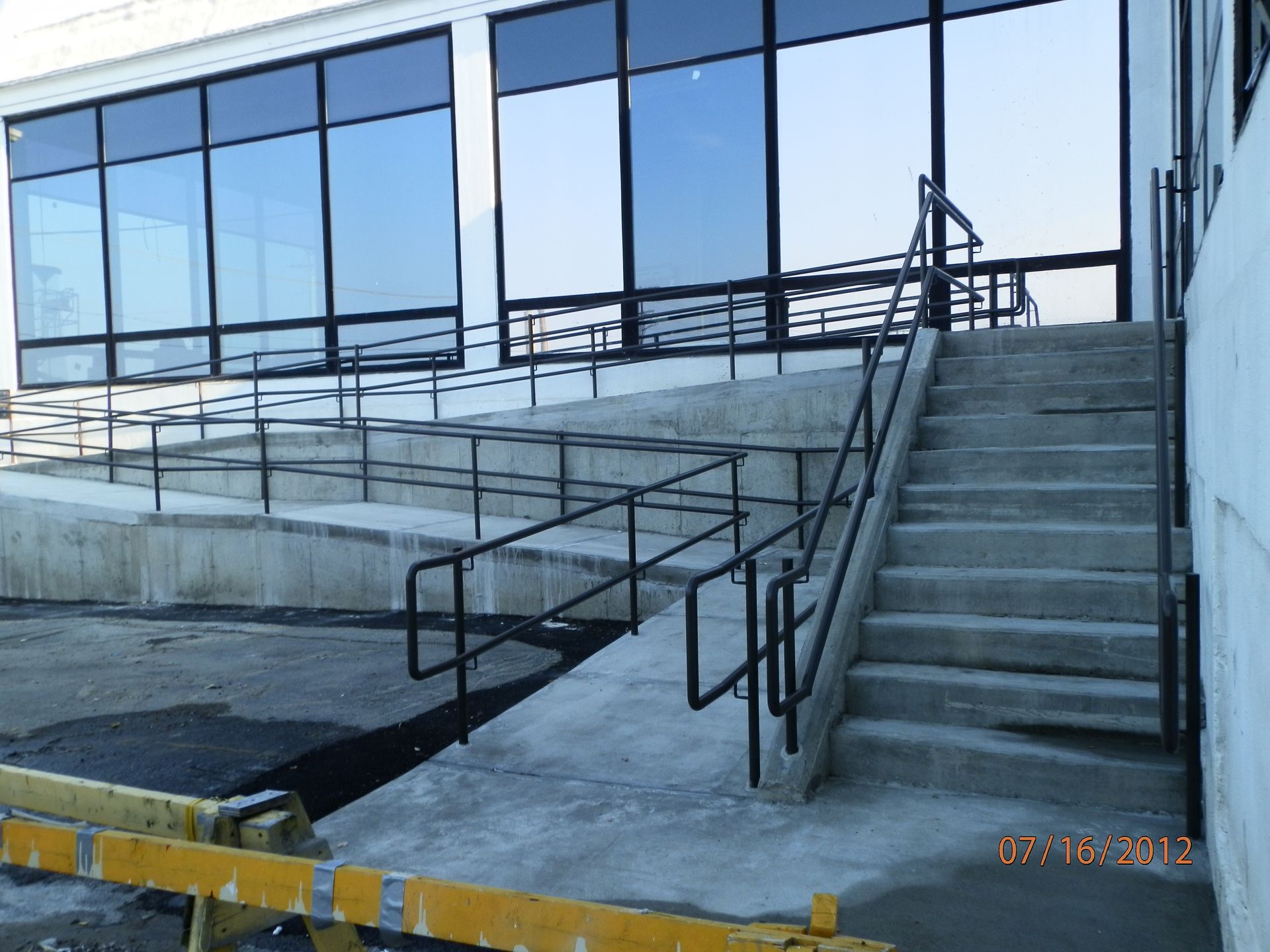 Exterior ramp and stairs leading to a building entrance with metal railings and glass windows.