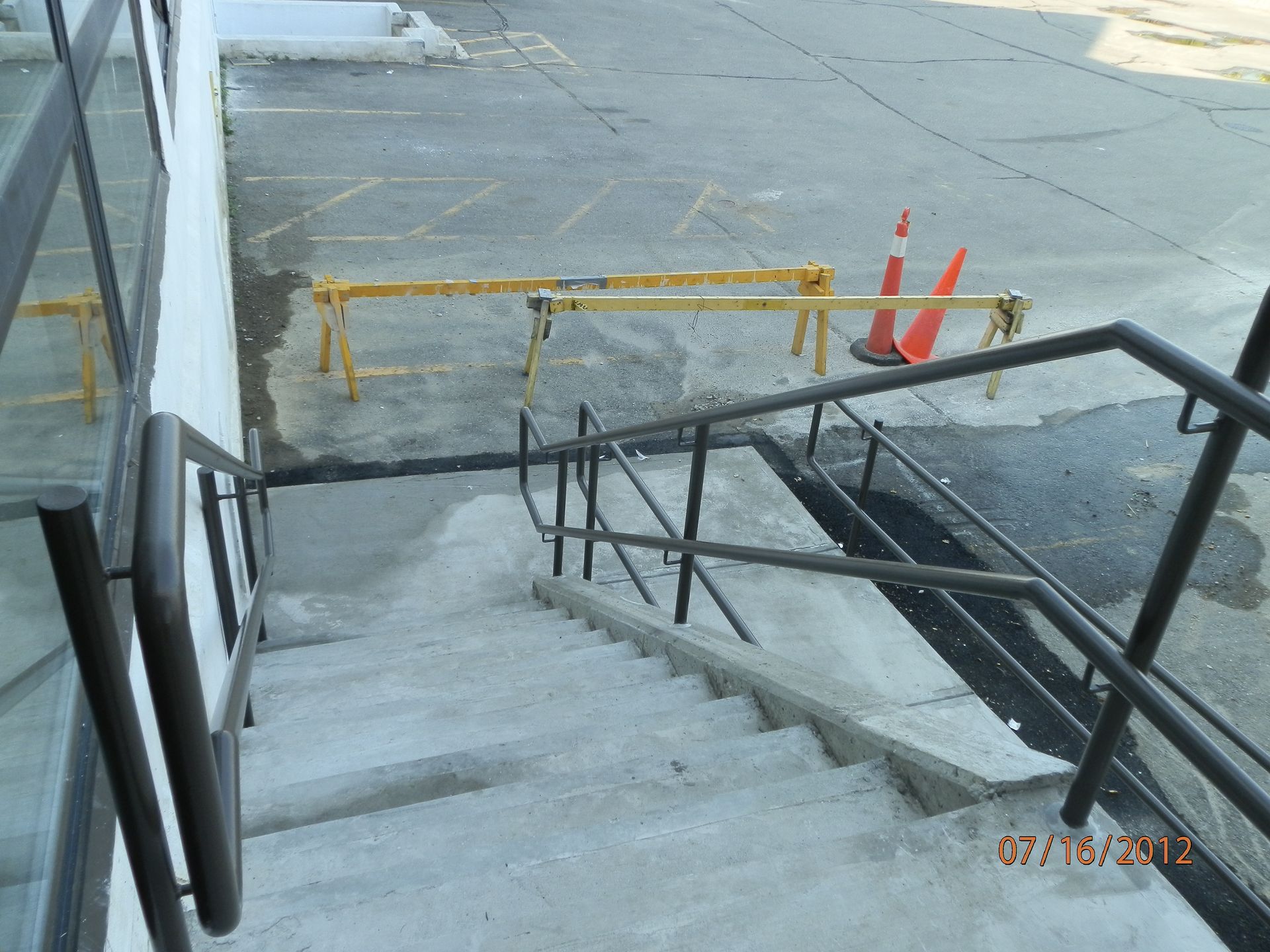 Stairway down to a parking lot with black handrails and yellow barrier tape blocking access.