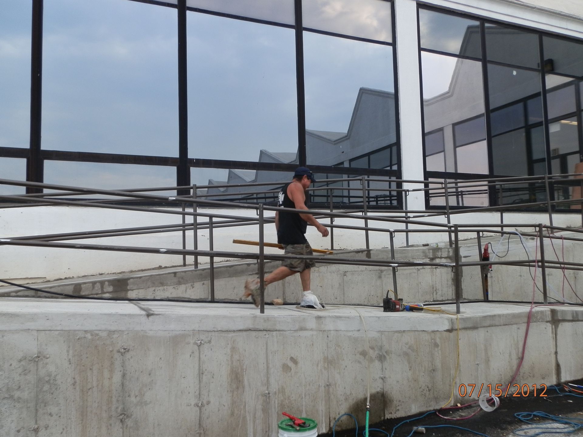Person walking on a concrete ramp beside a reflective glass building under a cloudy sky