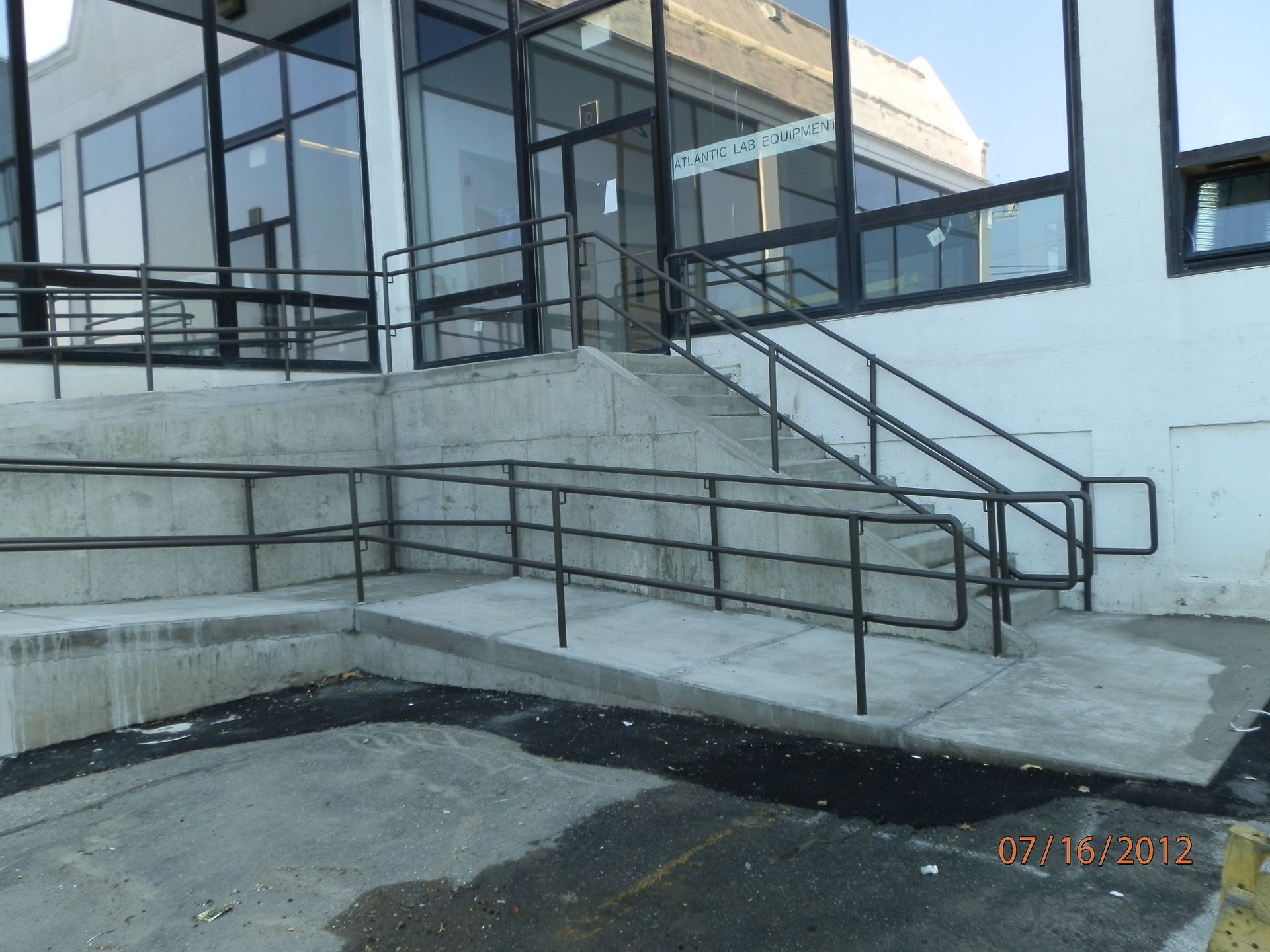 Concrete ramp and stairs leading to a glass-front building entrance with metal railings.