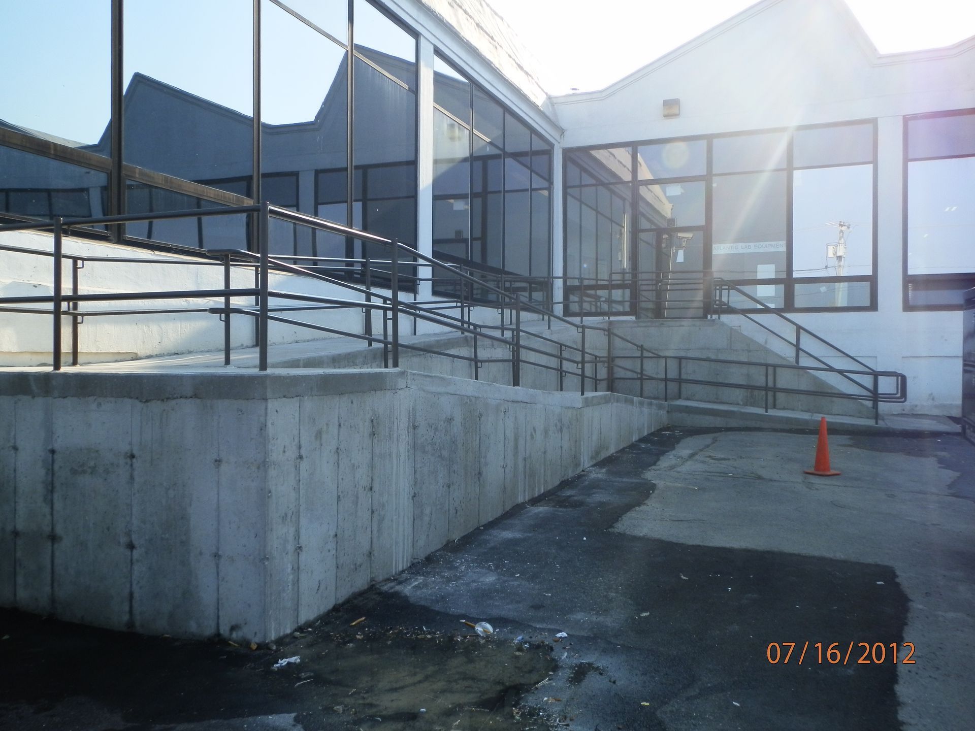 Concrete outdoor walkway and ramp beside a modern building with glass windows and an orange traffic cone