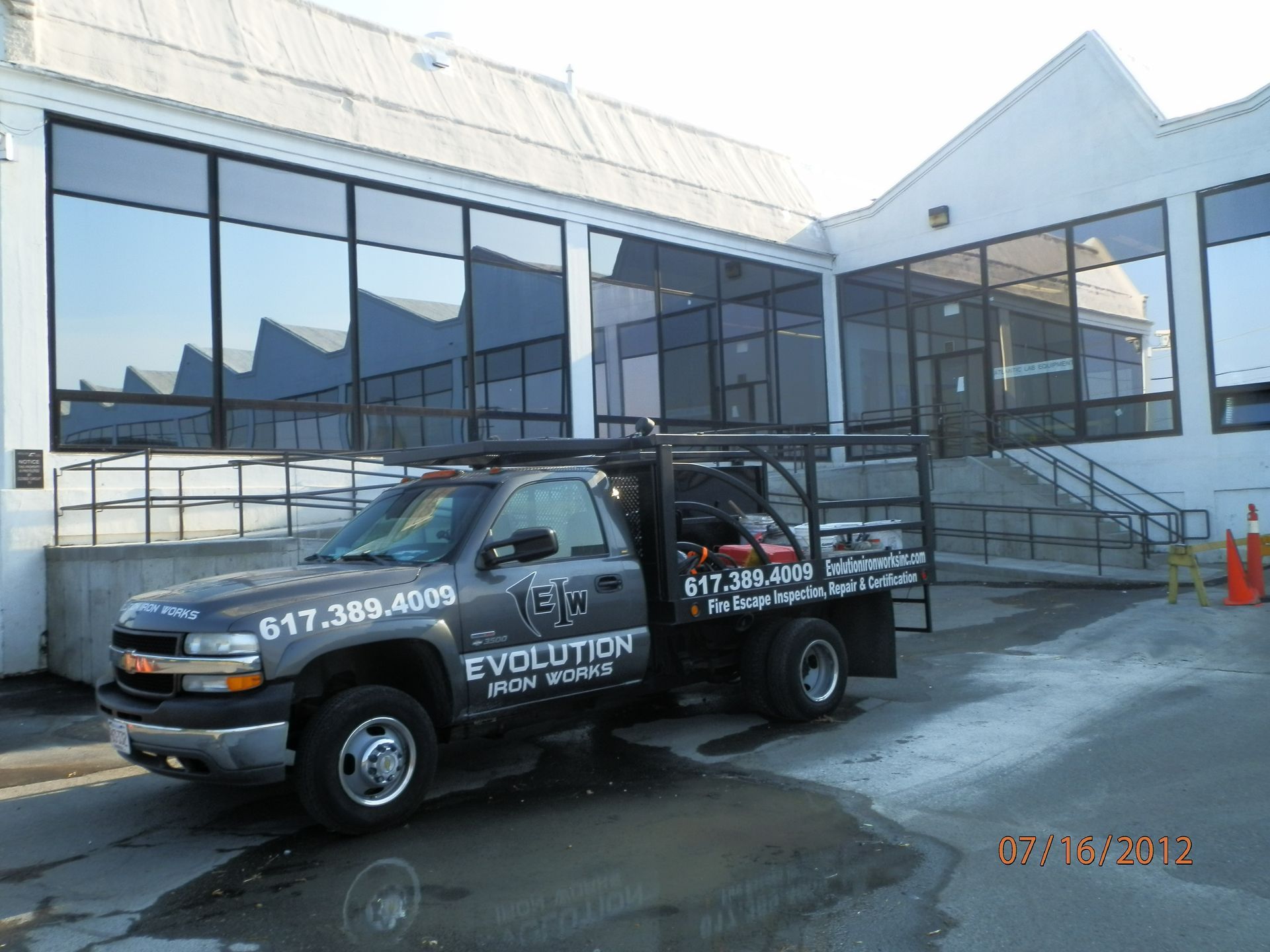 Black work van parked outside a glass-front building with steps and snow on the ground