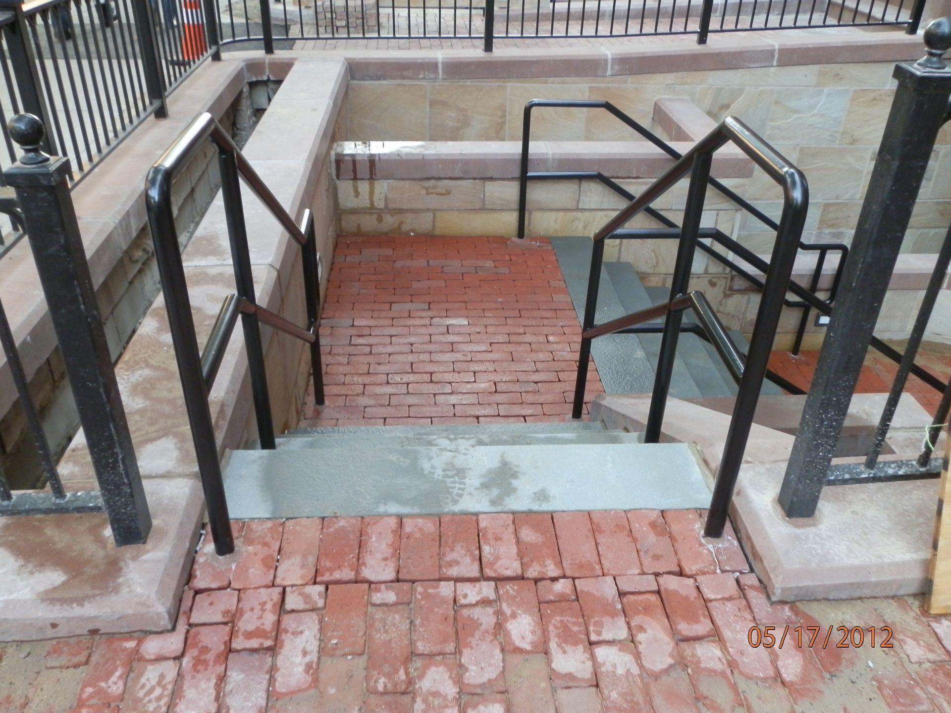 Brick stairway with black metal railings leading down to a lower landing outdoors.