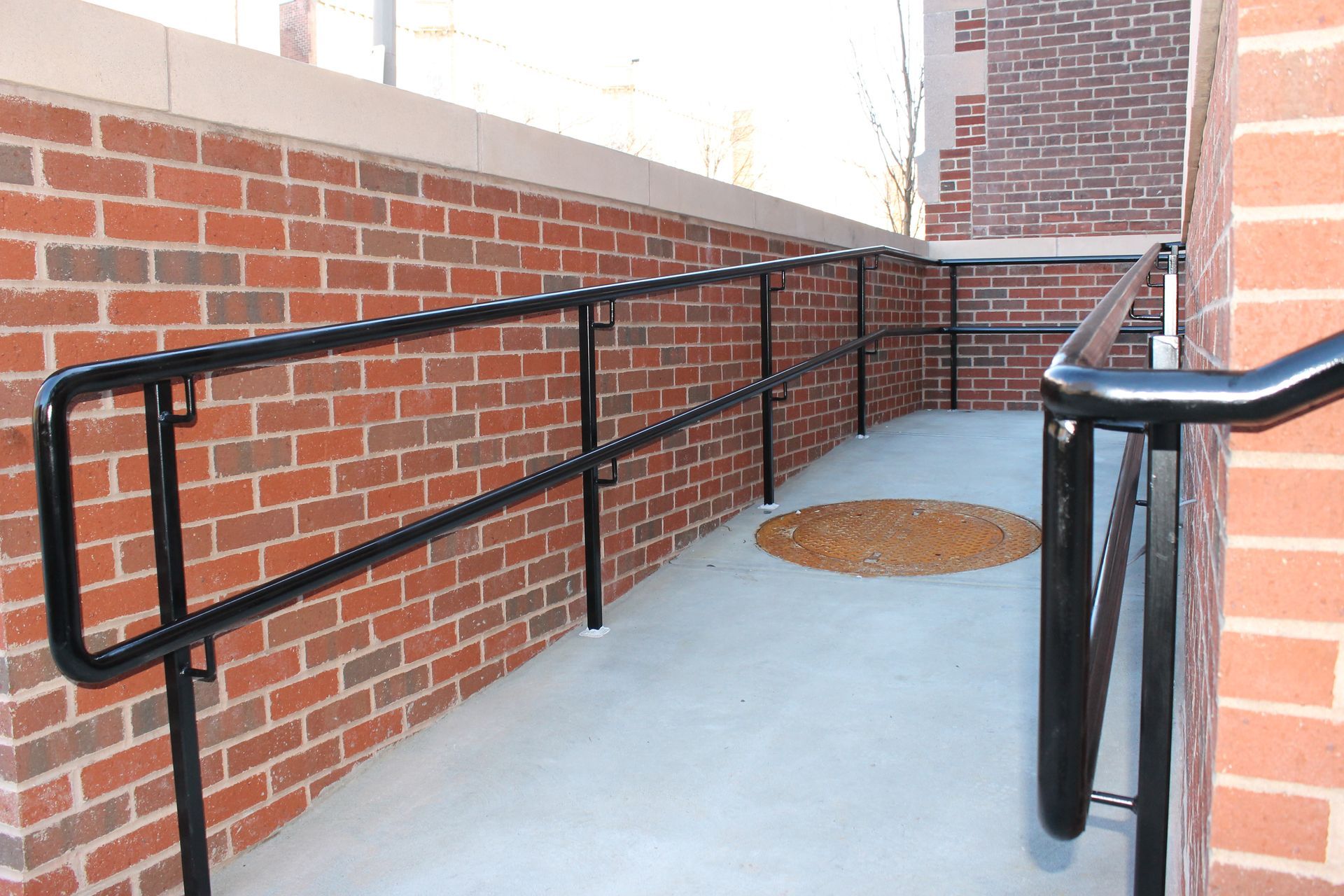 Concrete ramp with black handrails beside a red brick wall.