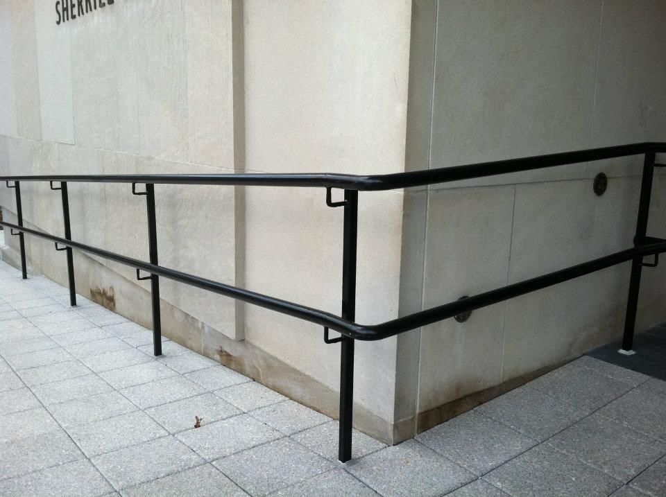 Black metal handrails line an accessible ramp beside a light stone building.