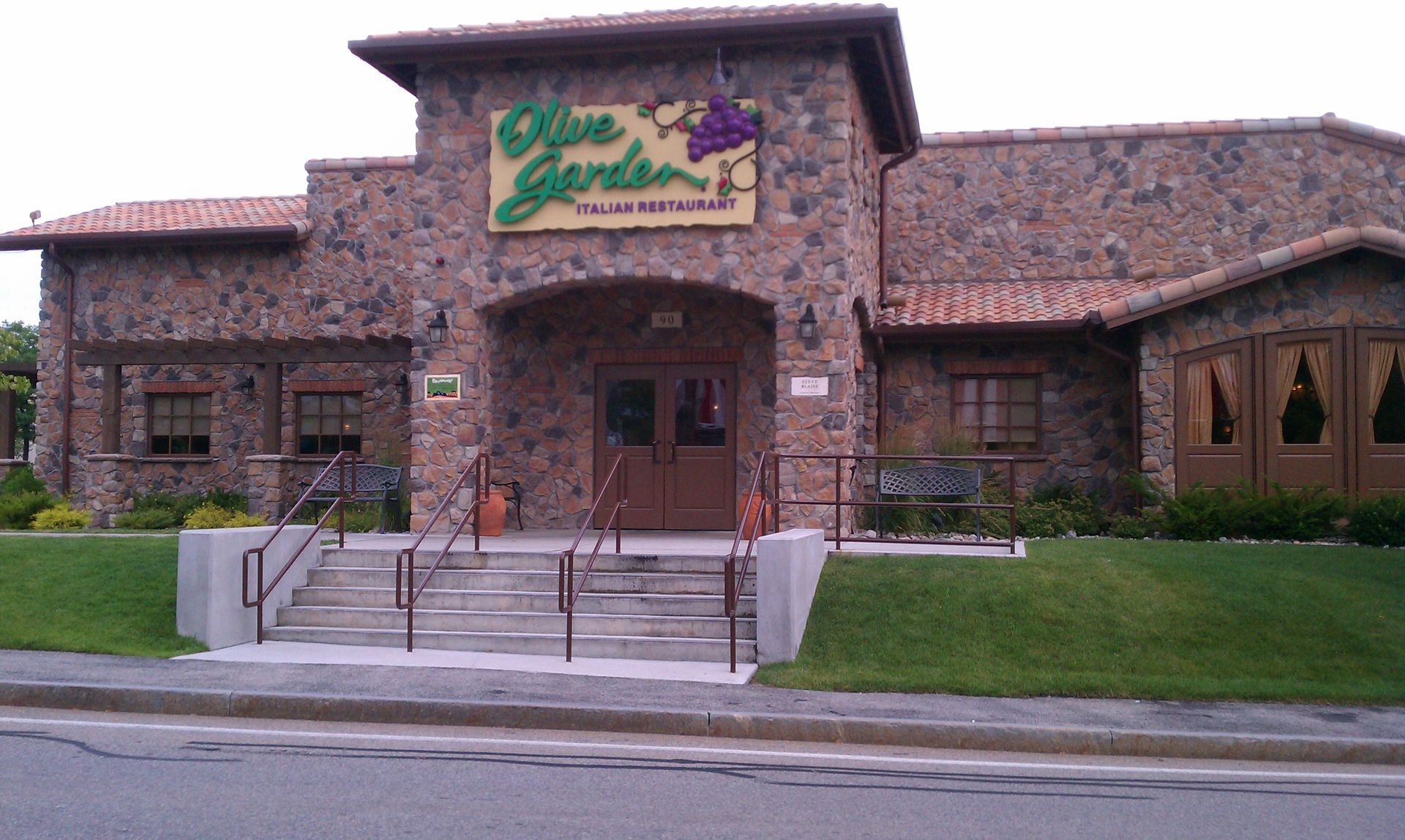 Stone restaurant building with green sign, front entrance, and manicured lawn by the street