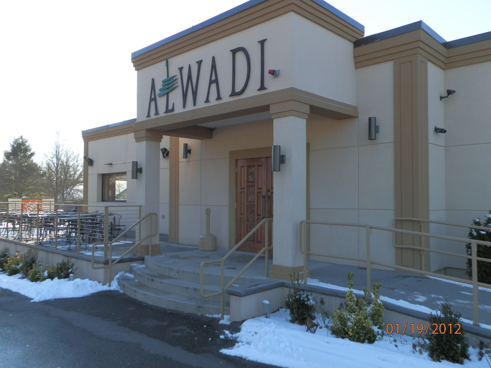Snowy entrance to the Alwadi building with steps, railings, and tan exterior walls.