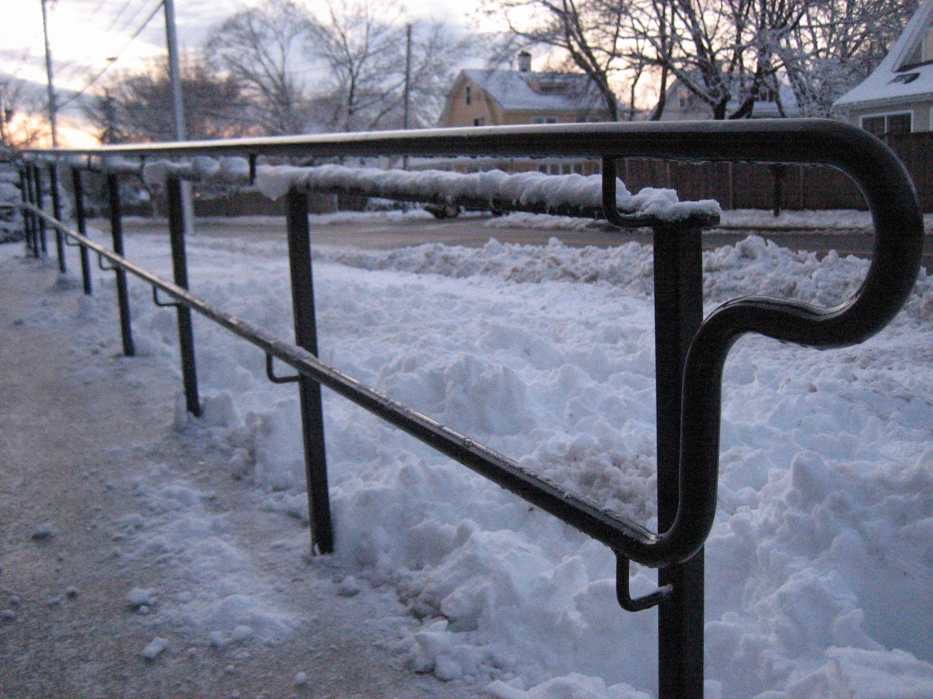 Snow-covered walkway with black metal handrail beside an icy path at dusk