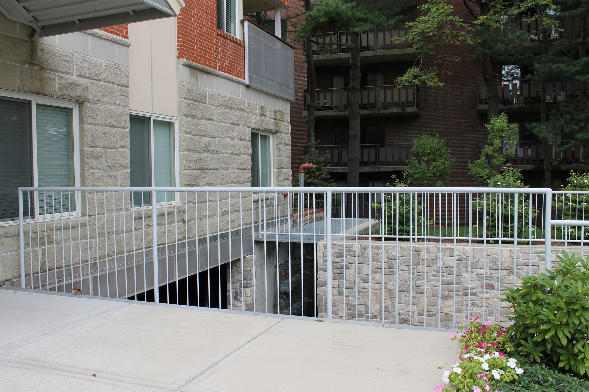 Apartment walkway with white railing and a stairwell beside a brick building and stone courtyard