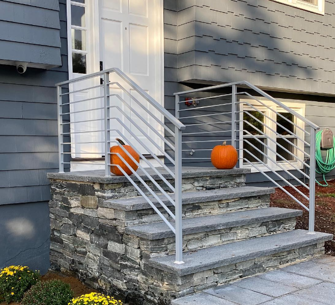 Brick porch steps with white metal handrails and pumpkins on the stoop on both sides and a grey house exterior