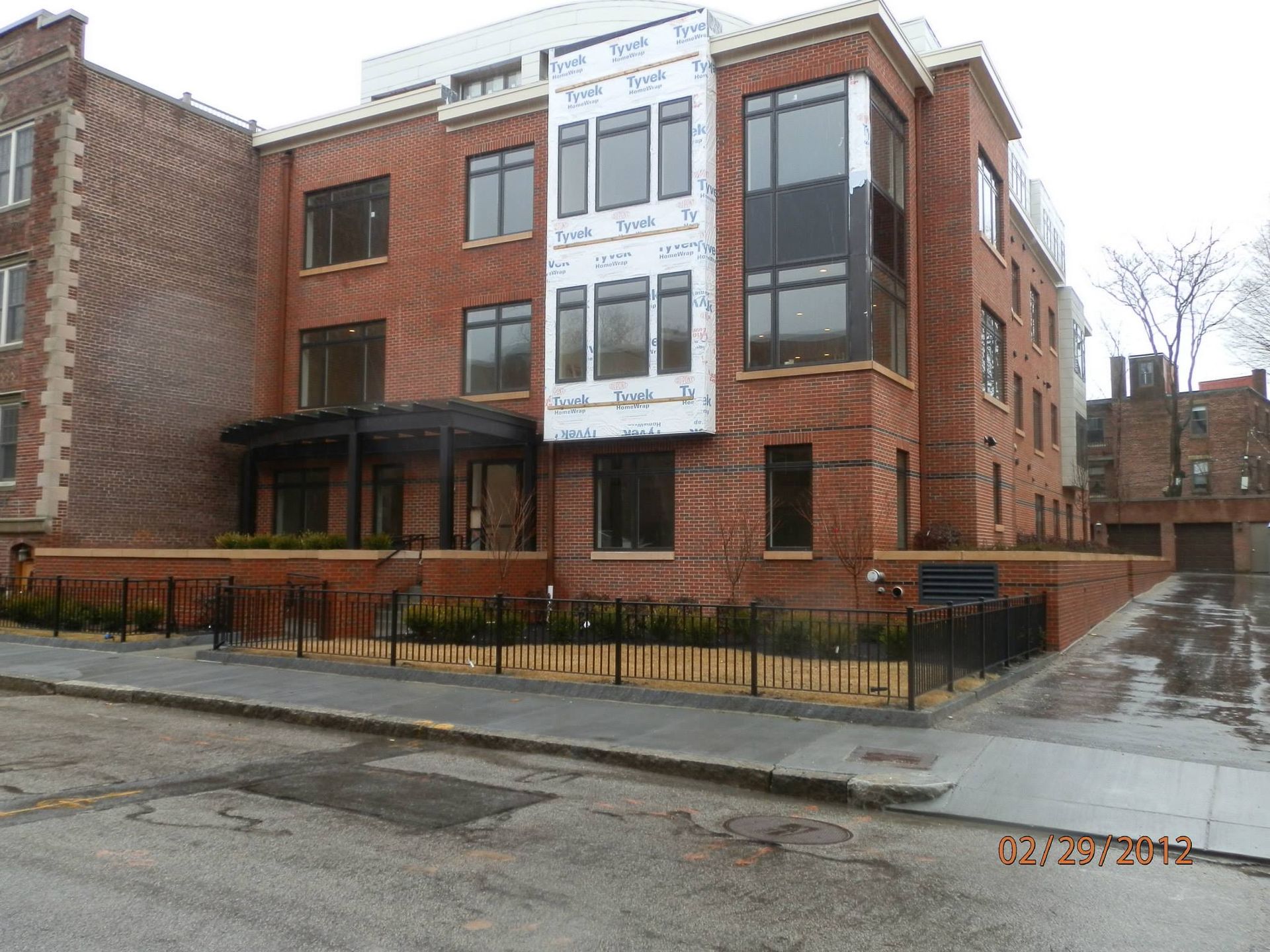 Brick apartment building with a white center section and metal railings on a wet street corner.