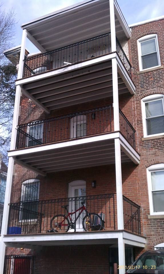 Brick apartment building with stacked balconies, black railings, and a red bicycle on the lower balcony