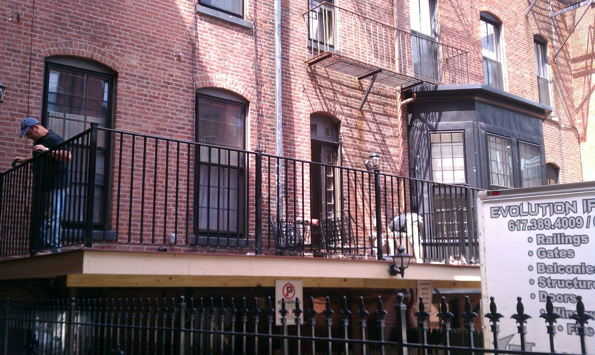 Brick apartment building with black balconies, a person on the left, and a sign with text on the right