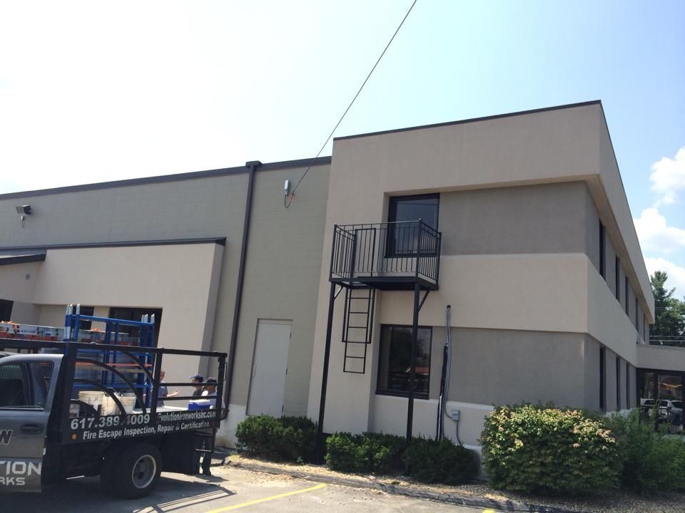 Exterior of a beige commercial building with a black metal staircase and service truck parked beside it