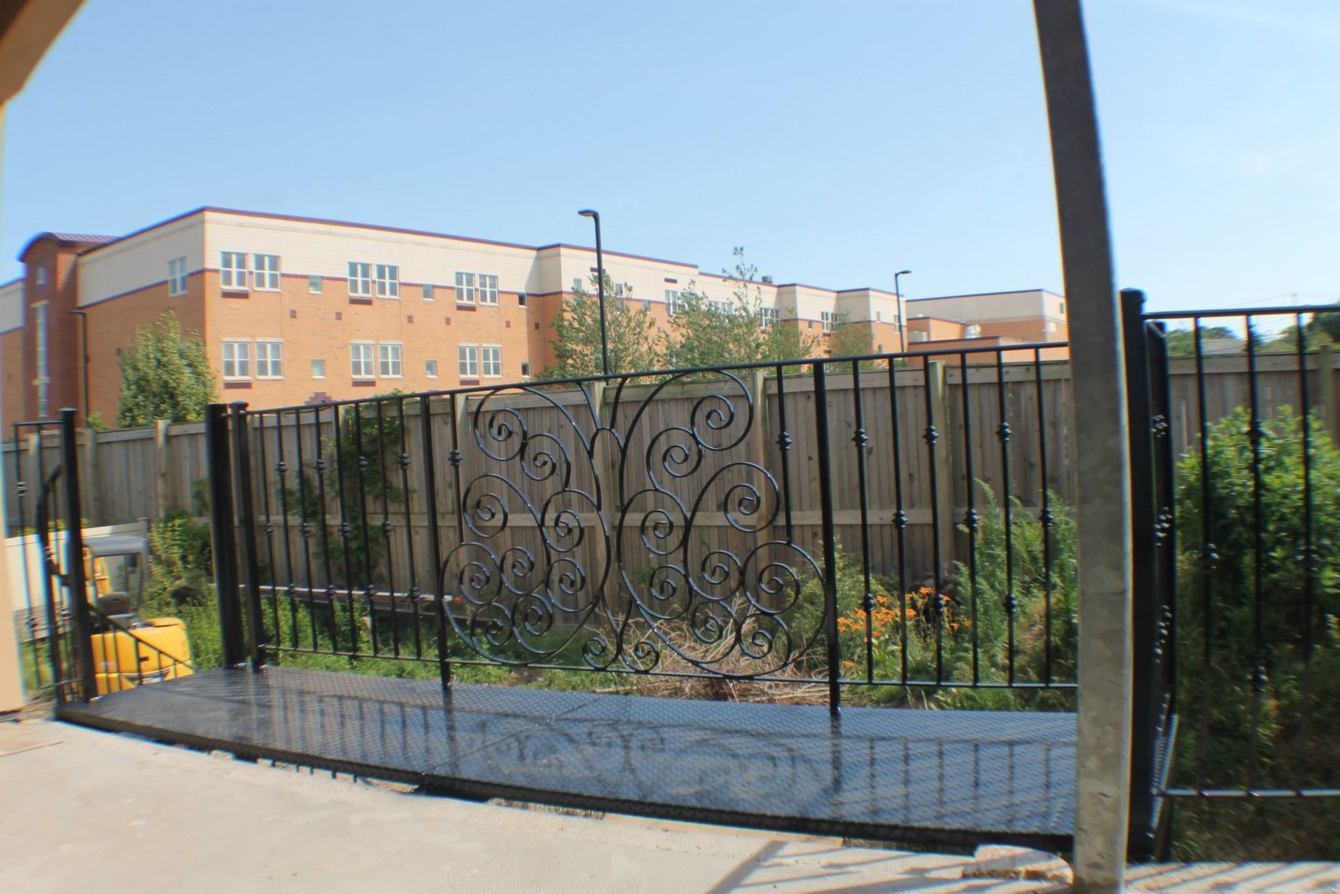 Black metal fence and gate in front of a brick apartment building on a sunny street.
