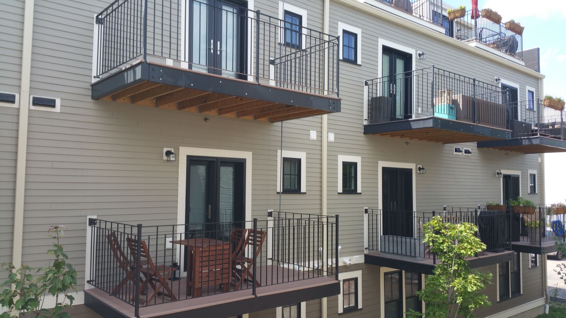 Apartment building balconies with black railings and sliding glass doors along a beige exterior