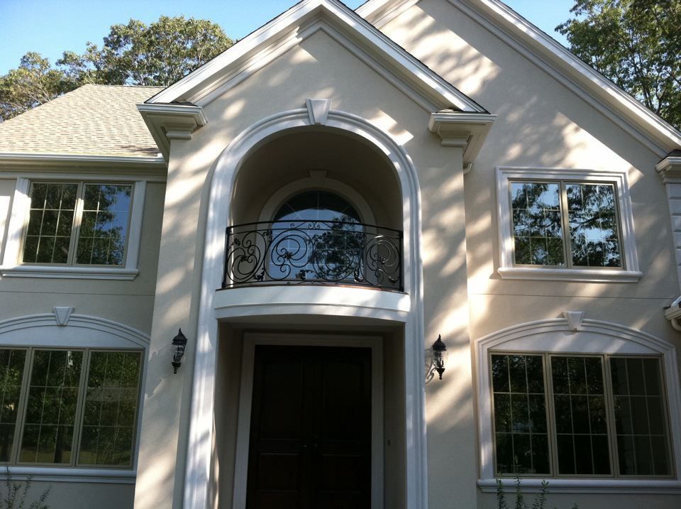 Front view of a white stucco house with arched entryway and black balcony railings