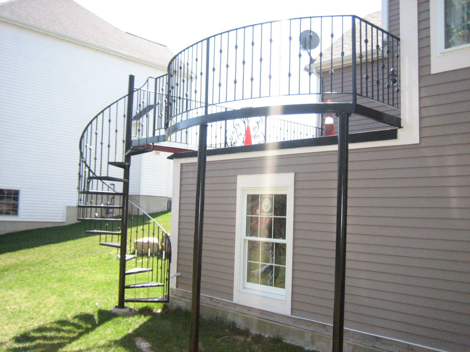 Spiral staircase leading to a raised deck on the side of a gray house with a grassy yard