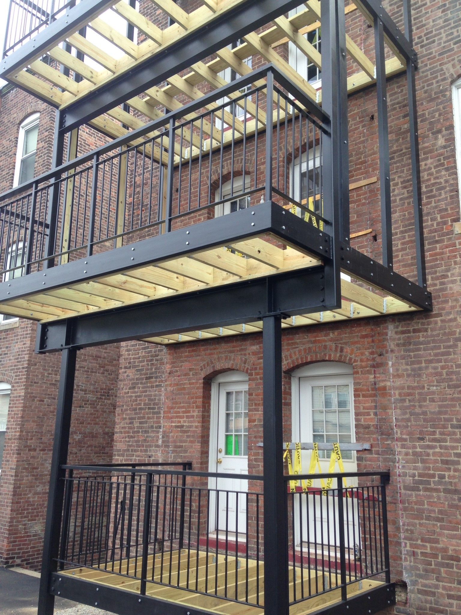 Brick building with black metal balconies and railings, viewed from below.
