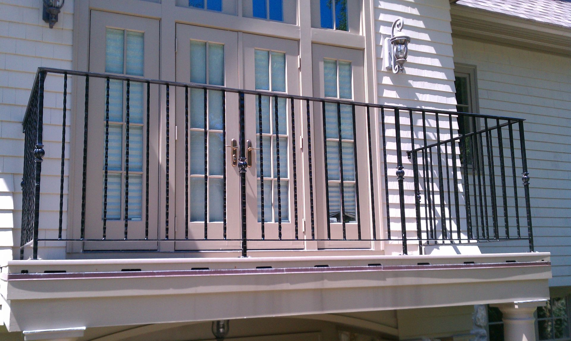 Small balcony with black metal railing in front of double glass doors and white siding.