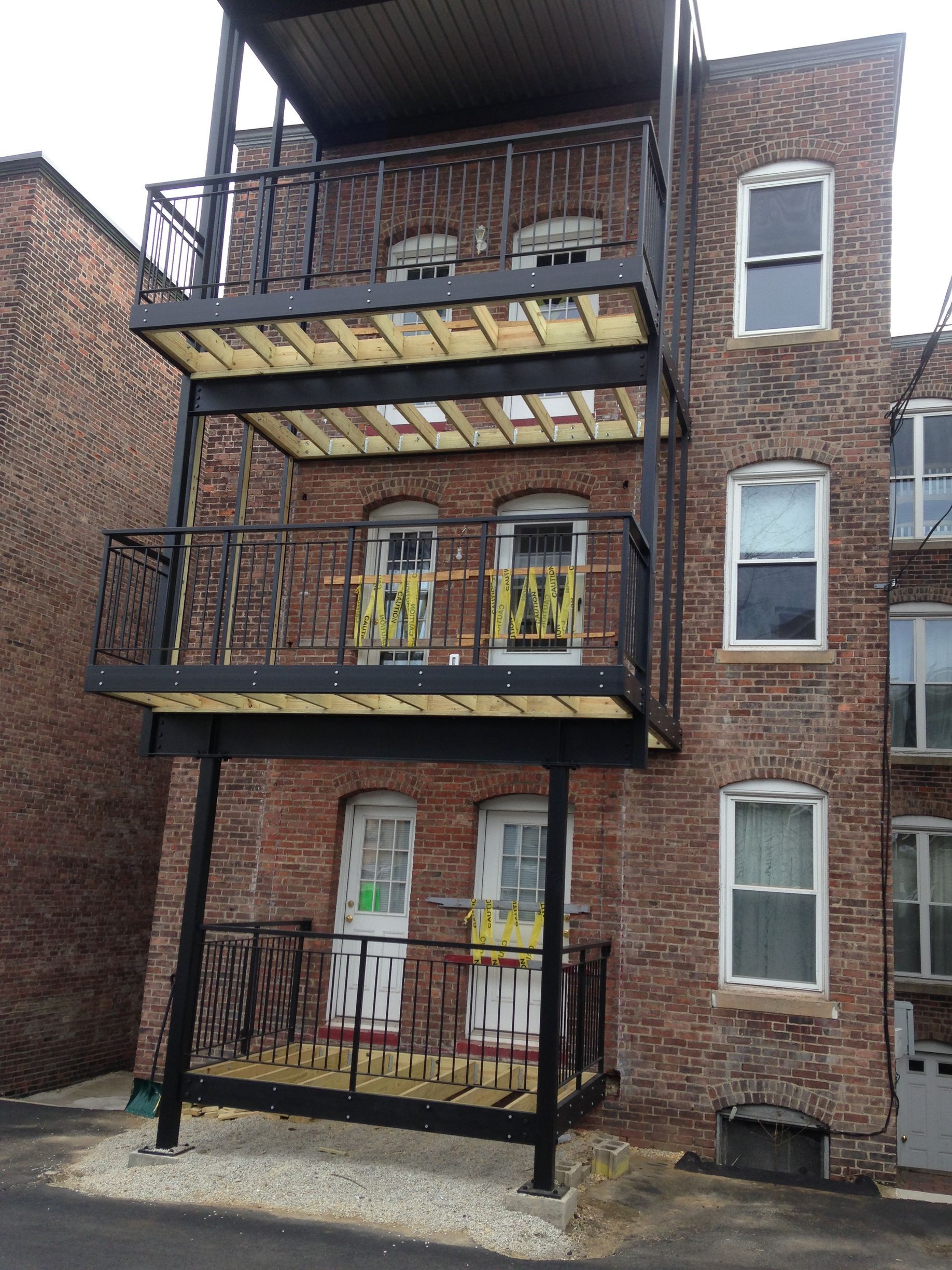 Brick apartment building with three stacked fire escapes and balconies facing a narrow alley