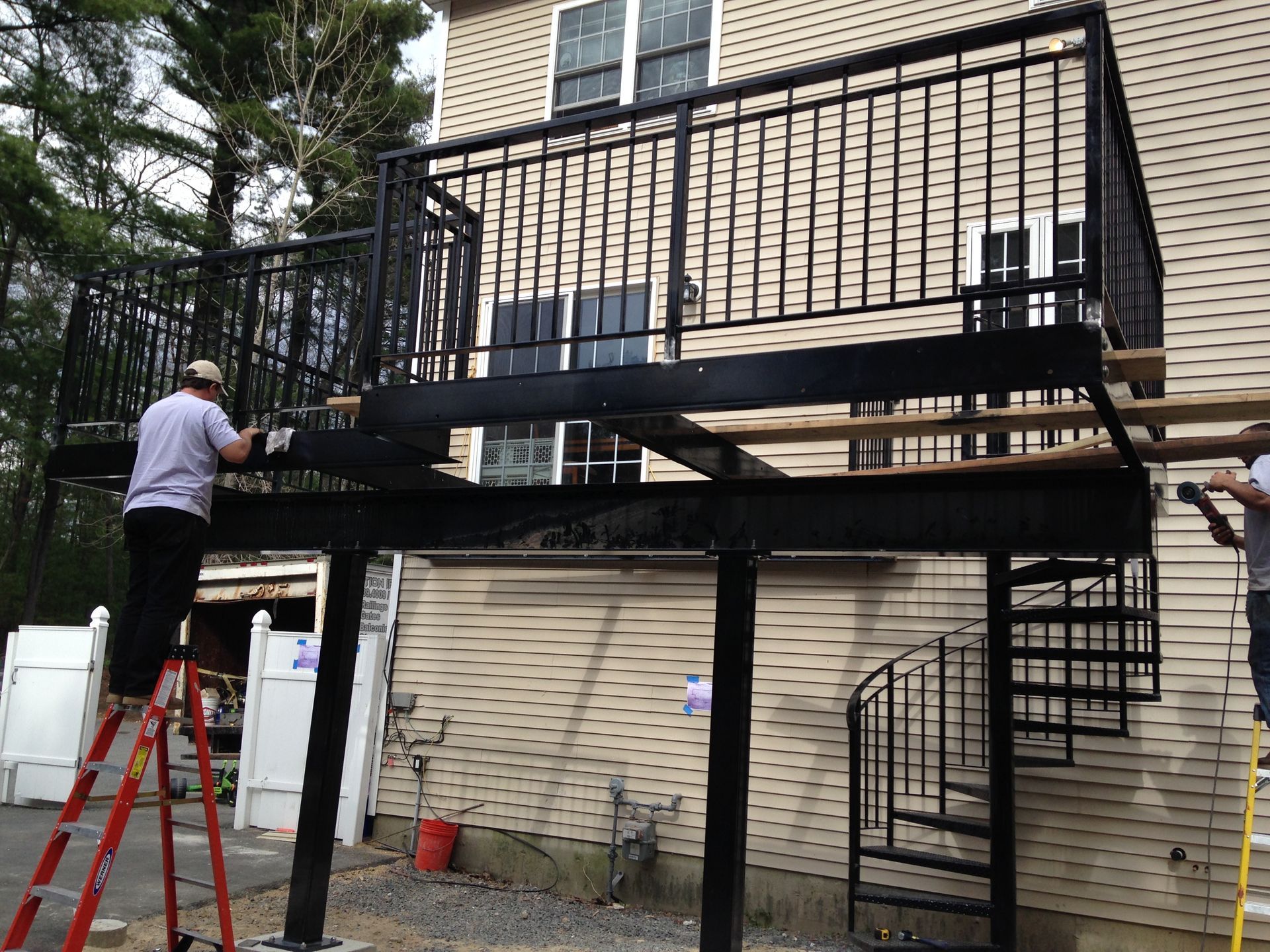 Worker installing a black metal staircase and balcony on a brick building exterior